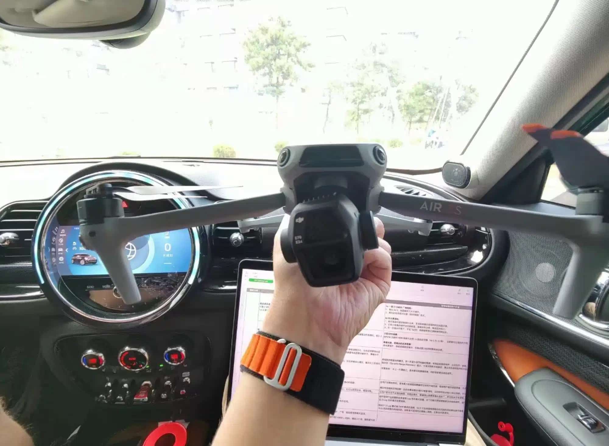 A hand holds the folded Air 3S inside a car above a laptop of specs.