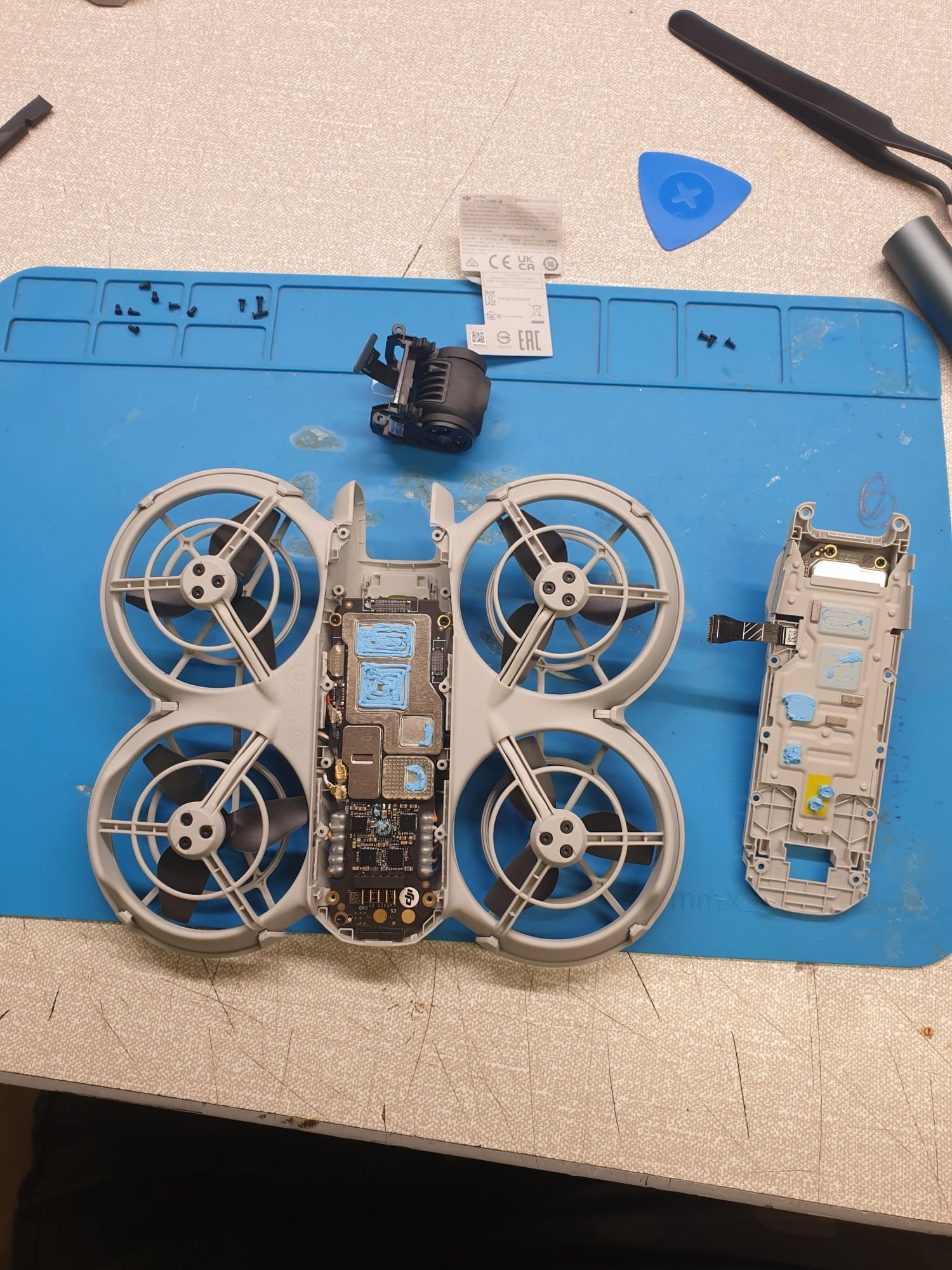 Disassembled DJI Neo laid open on a blue repair mat beside its shell.