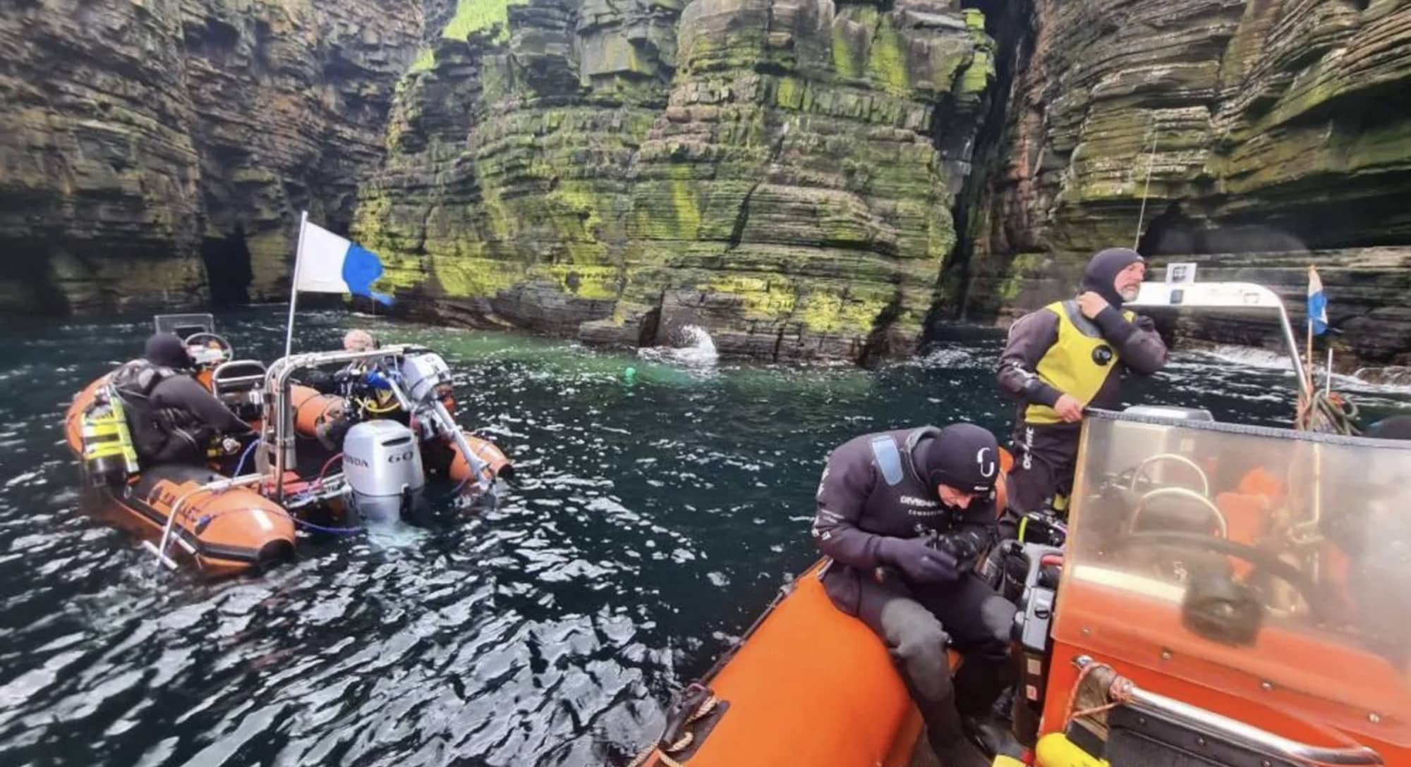 Divers aboard orange inflatable boats below towering Caithness sea cliffs.