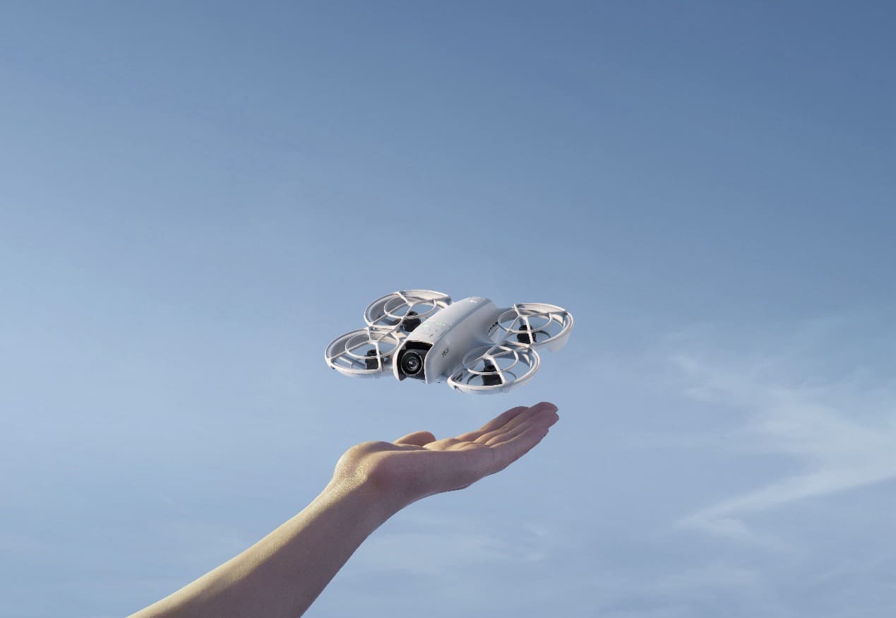 The Neo hovers just above an open palm against a pale blue sky.