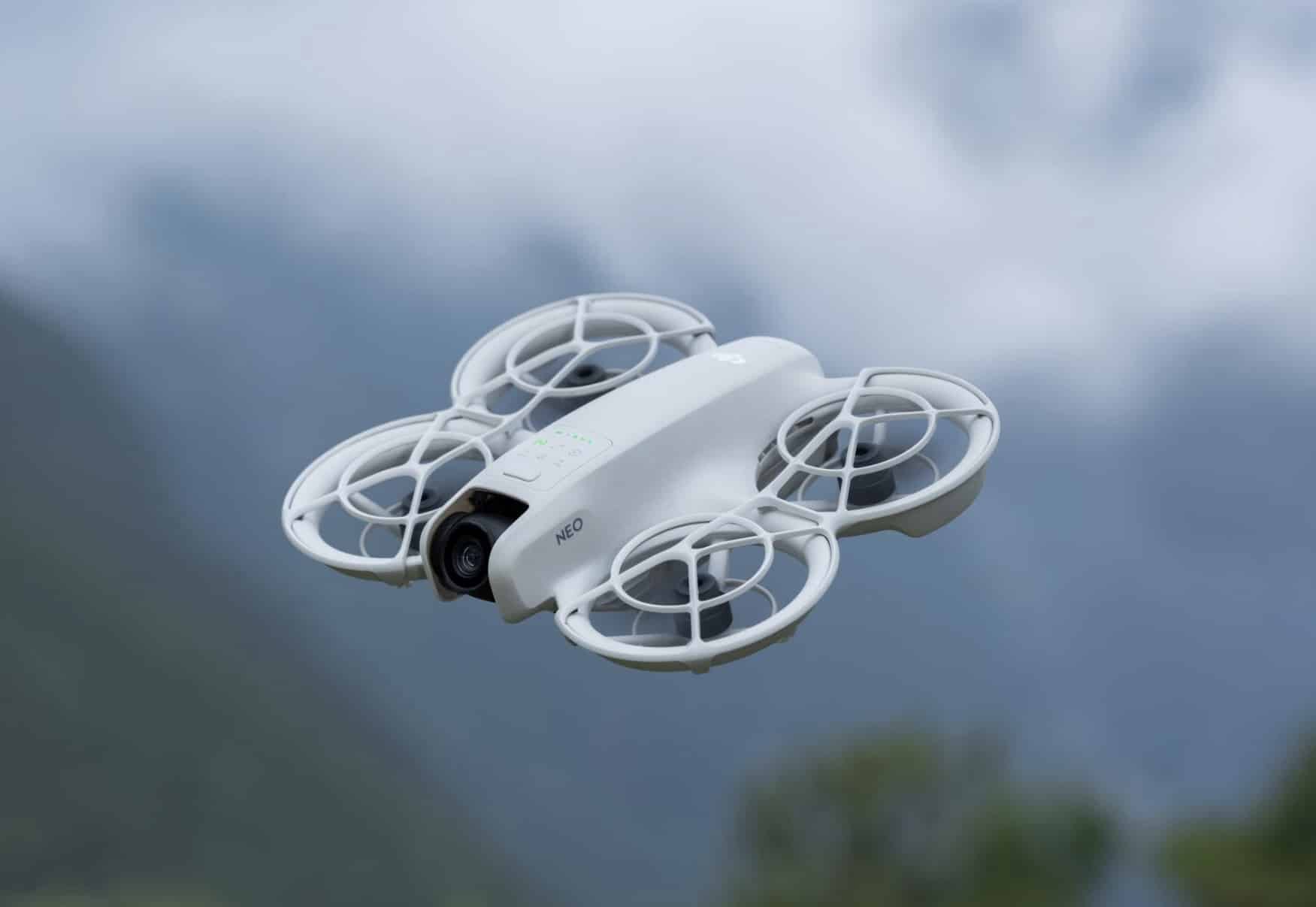 The DJI Neo banks through hazy air above a lake, propeller guards visible.