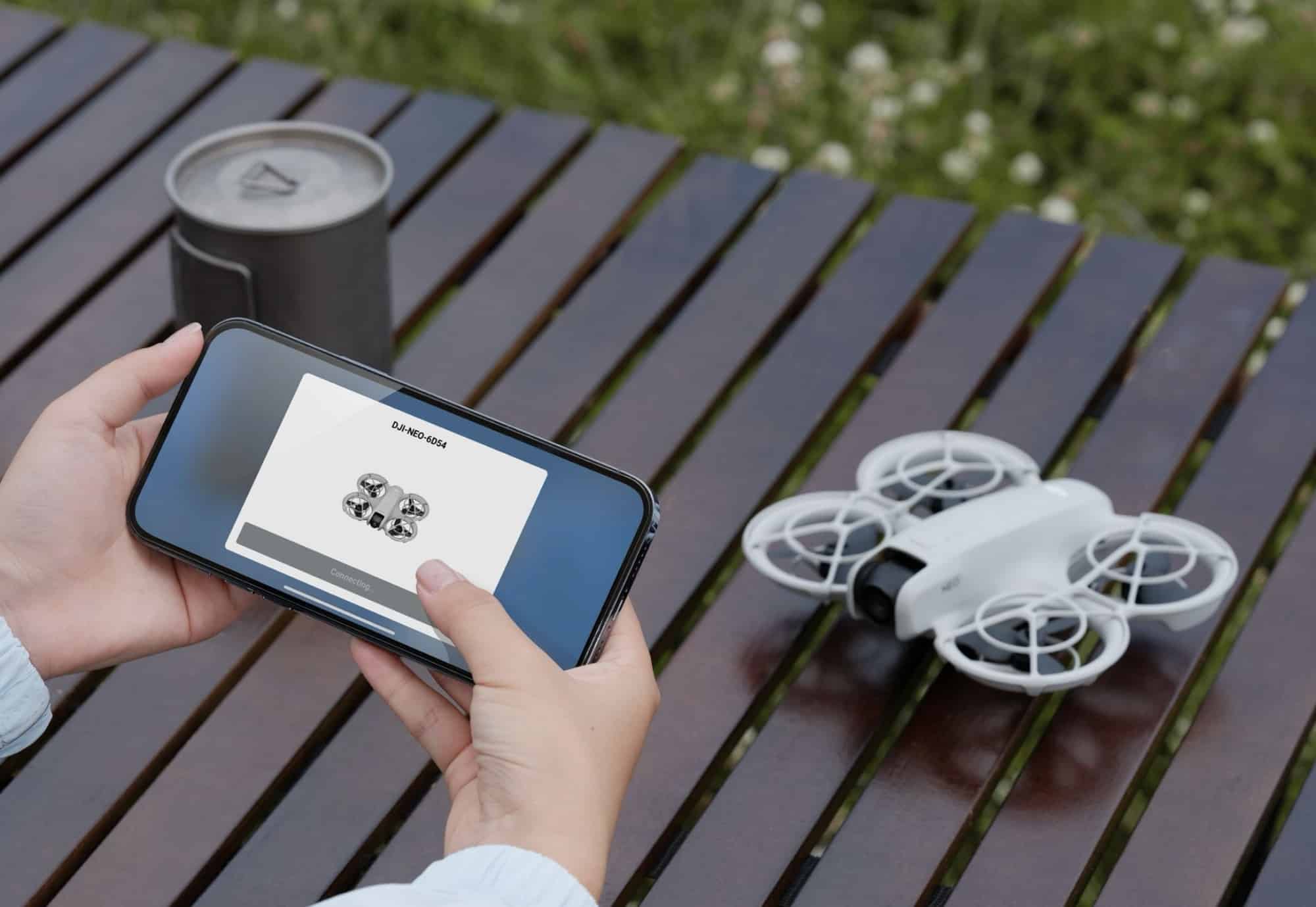 The Neo rests on a wooden table beside a phone running the DJI Fly app.
