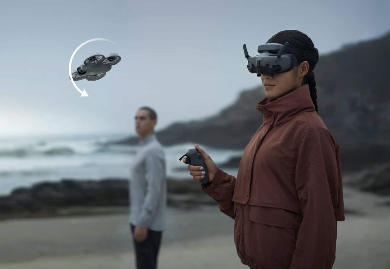 A woman in DJI Goggles flies the Neo by the coast using a motion controller.
