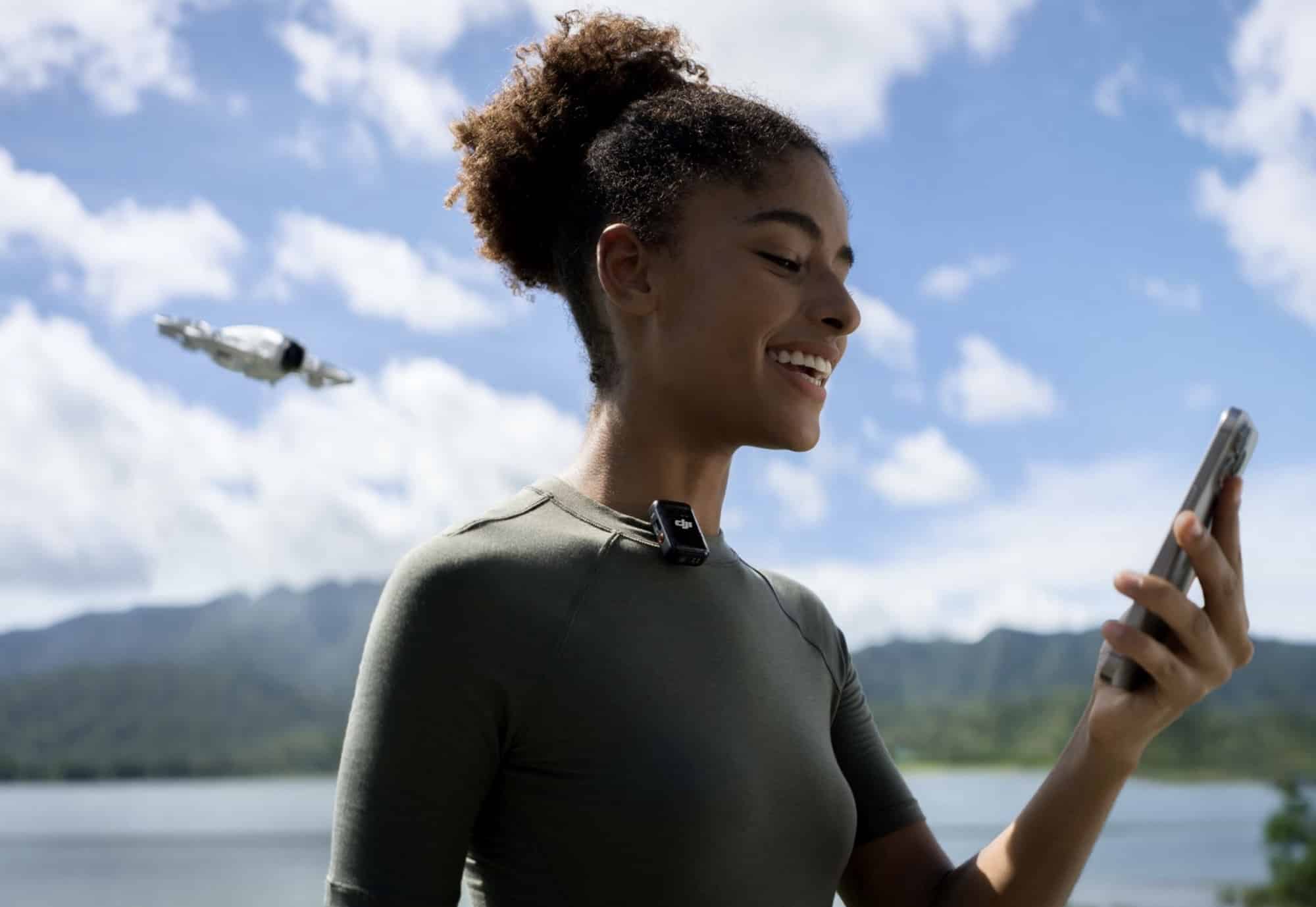 A woman in athletic wear checks her phone while the Neo hovers over the lake.