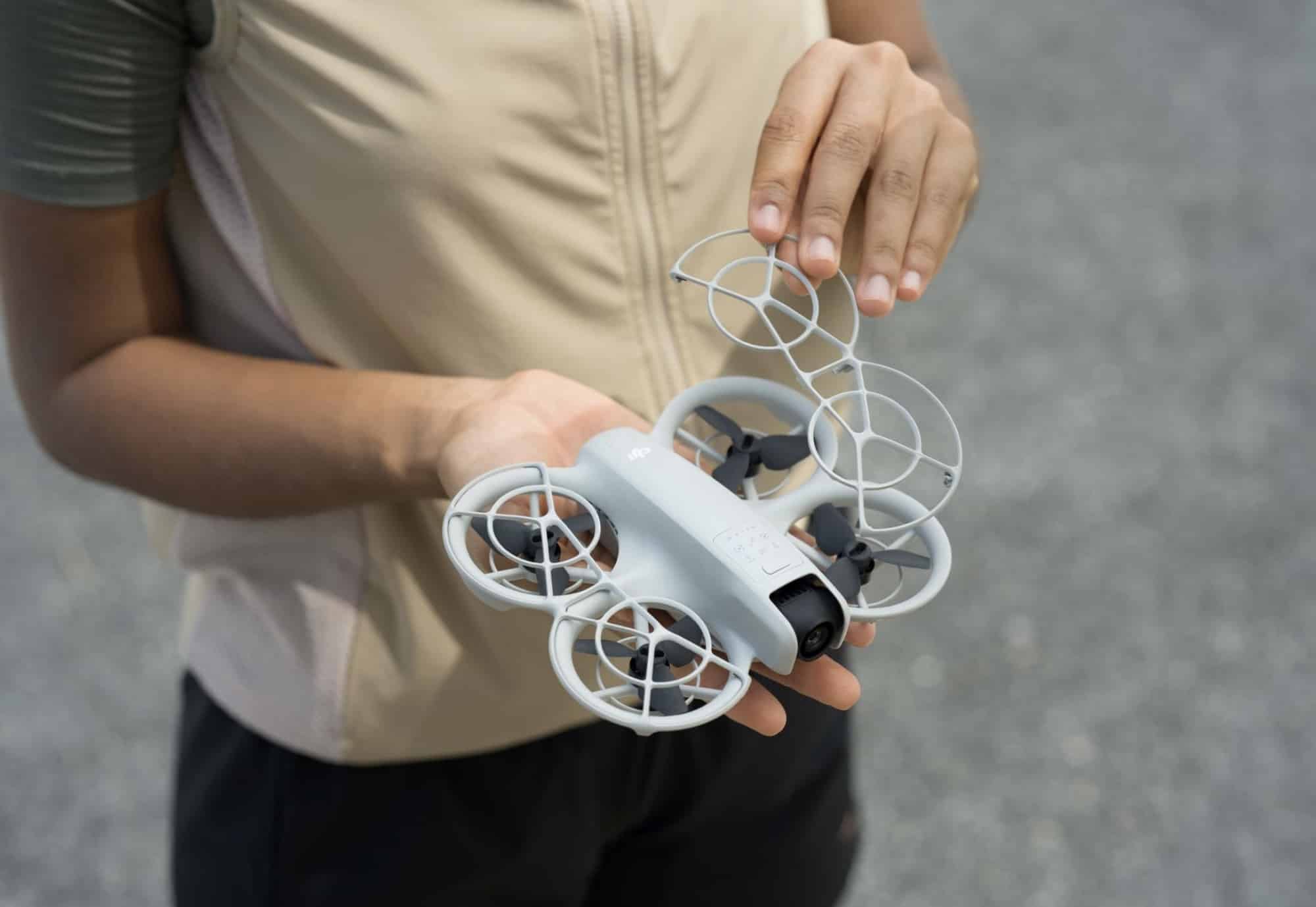 Hands cradle the palm-sized Neo, its four propeller guards clearly visible.