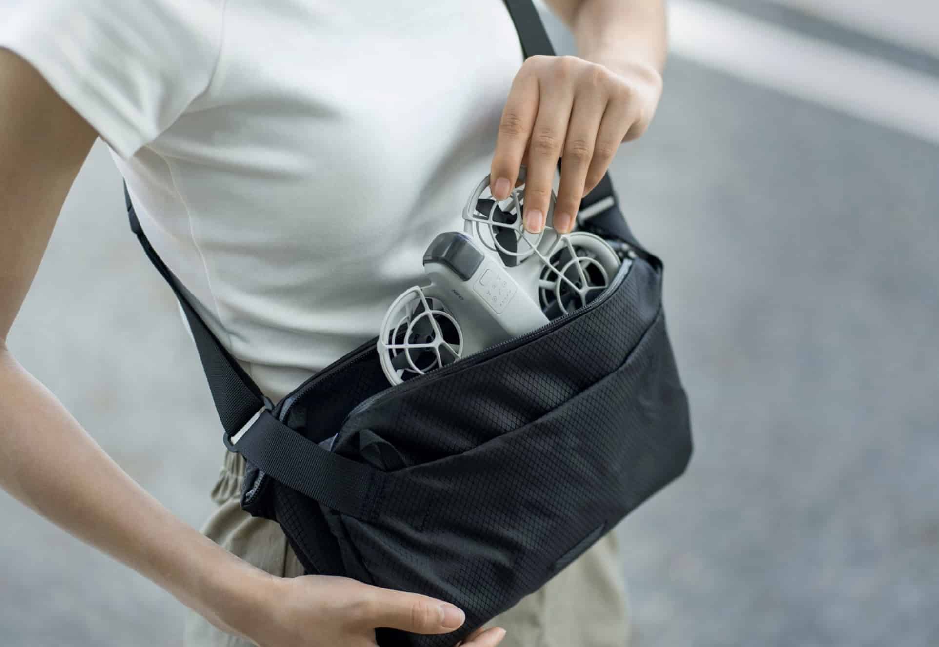 The Neo is lifted out of a black sling bag worn at the hip.