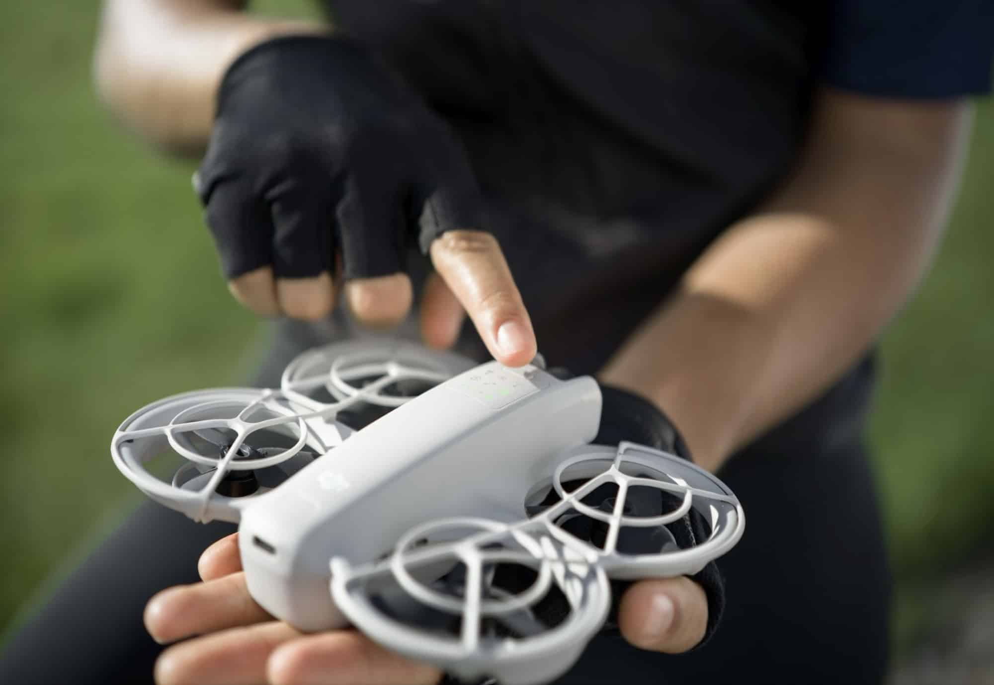 A gloved finger presses the Neo's mode button while holding the drone.