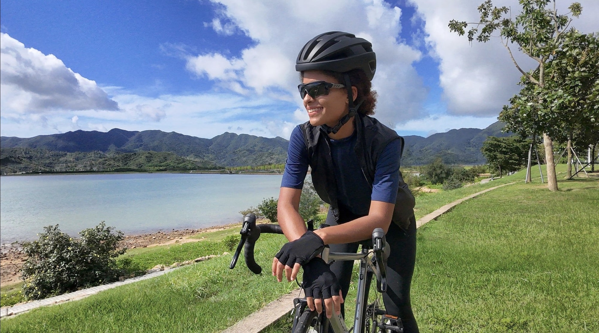 A helmeted road cyclist rides toward the Neo along a lakeside path.