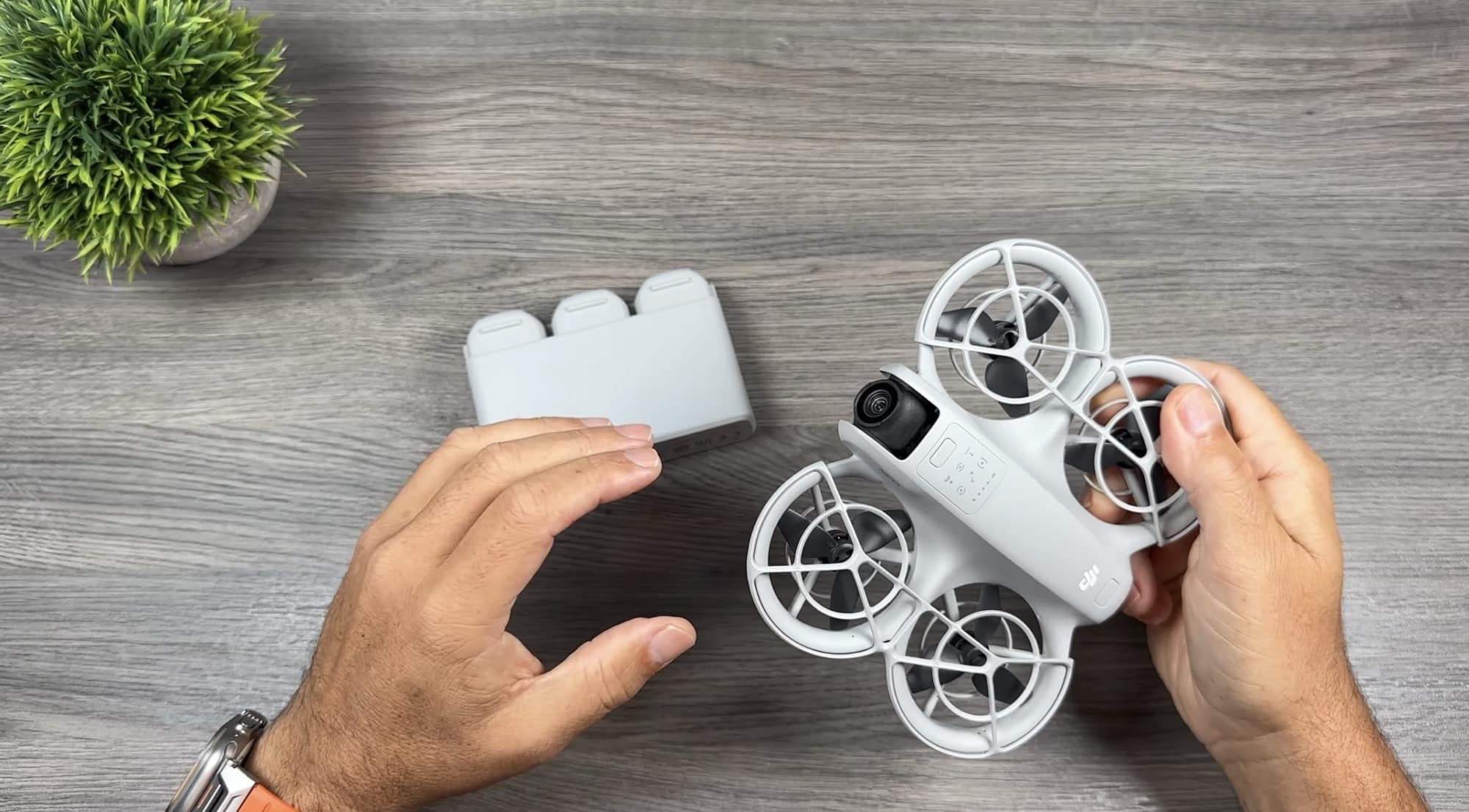 Hands lifting the battery out of the DJI Neo on a wooden table.