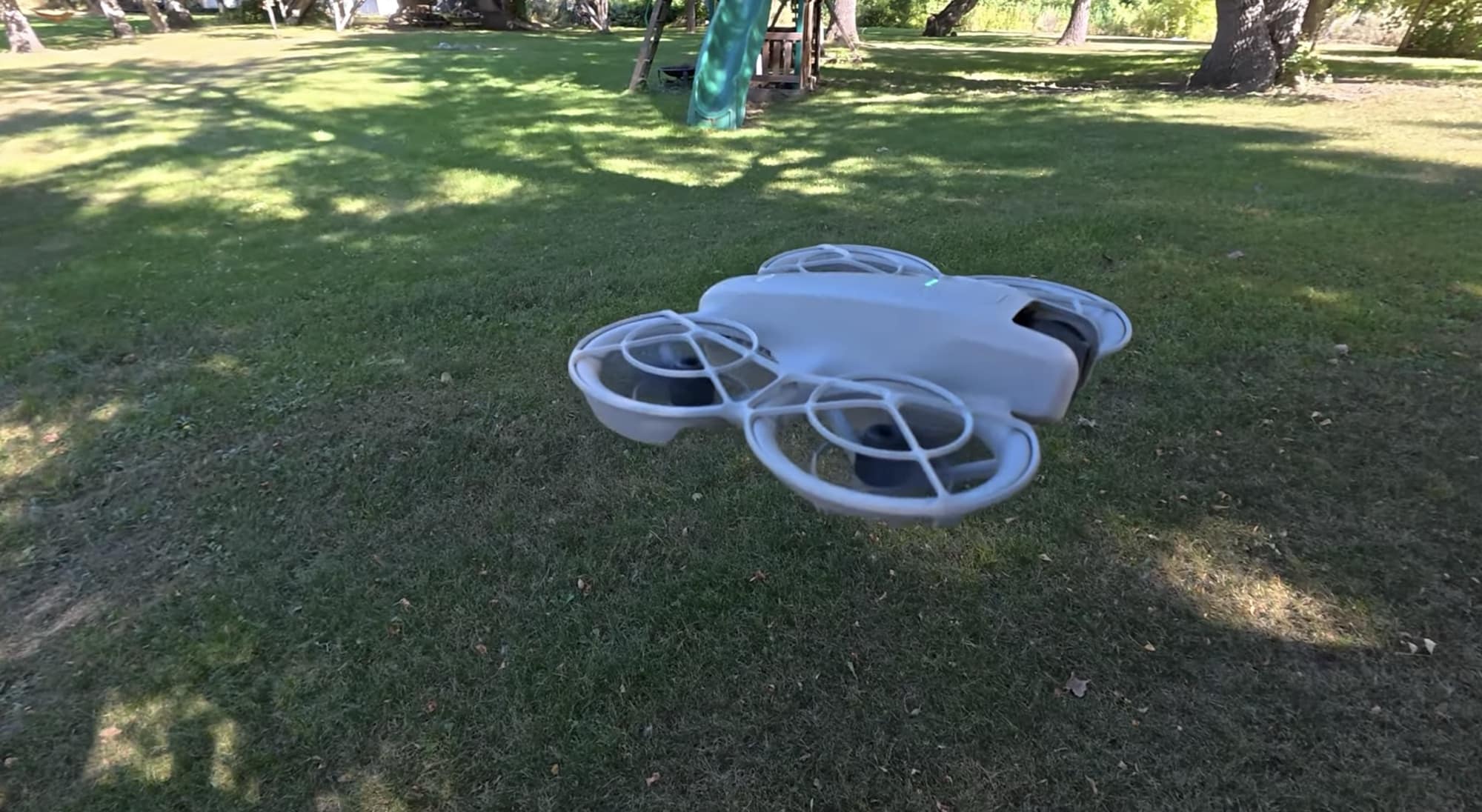 DJI Neo hovering just above the grass in a shaded backyard.
