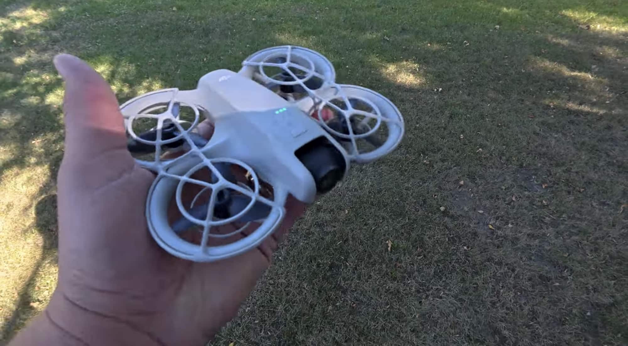 Hand holding the palm-sized DJI Neo with its ducted propeller guards.
