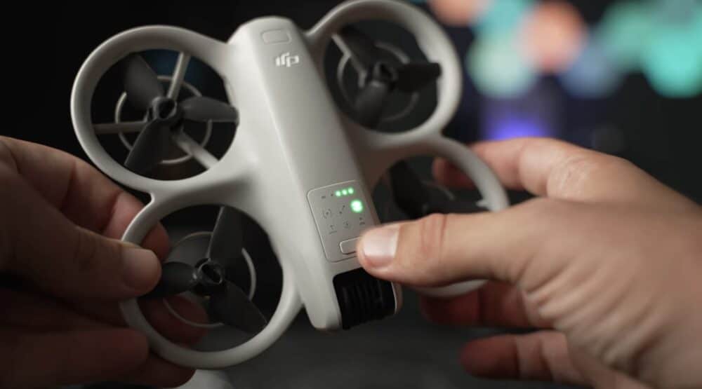 Hands hold the DJI Neo and press its mode button as the status light glows.