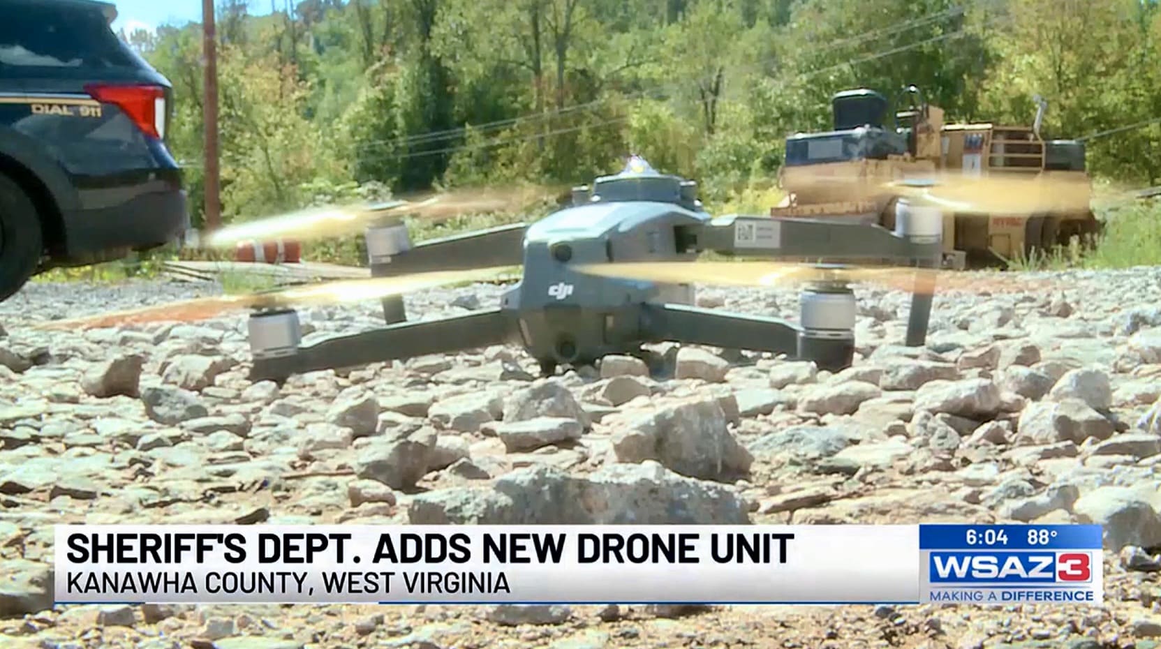 A DJI Mavic lifting off from a rocky riverbed beside a police vehicle.