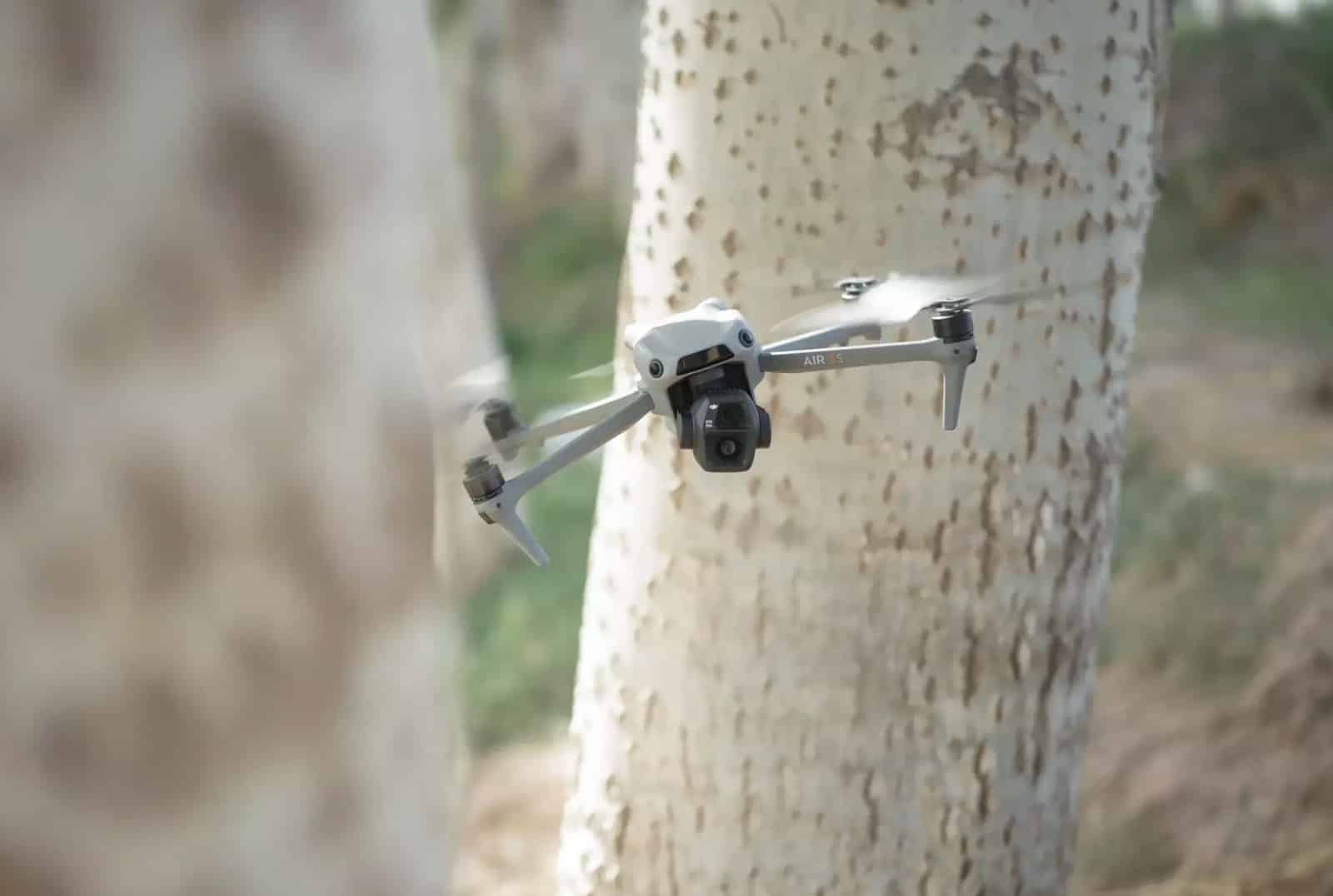 DJI Air 3S hovering close to a pale tree trunk in soft light.