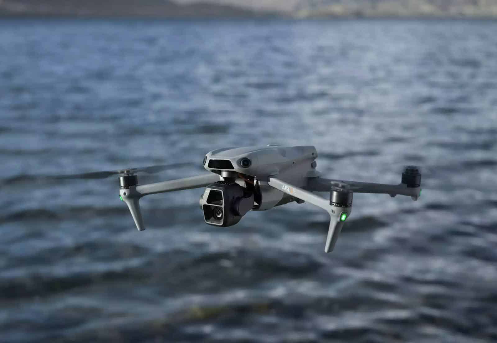 DJI Air 3S hovering just above choppy coastal water with its dual camera facing forward.