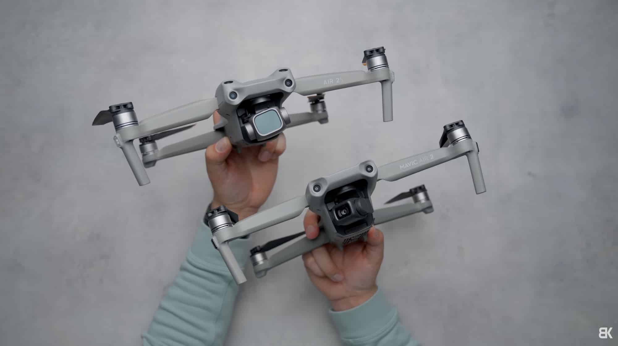 Two DJI Air-series drones held side by side over a concrete backdrop.