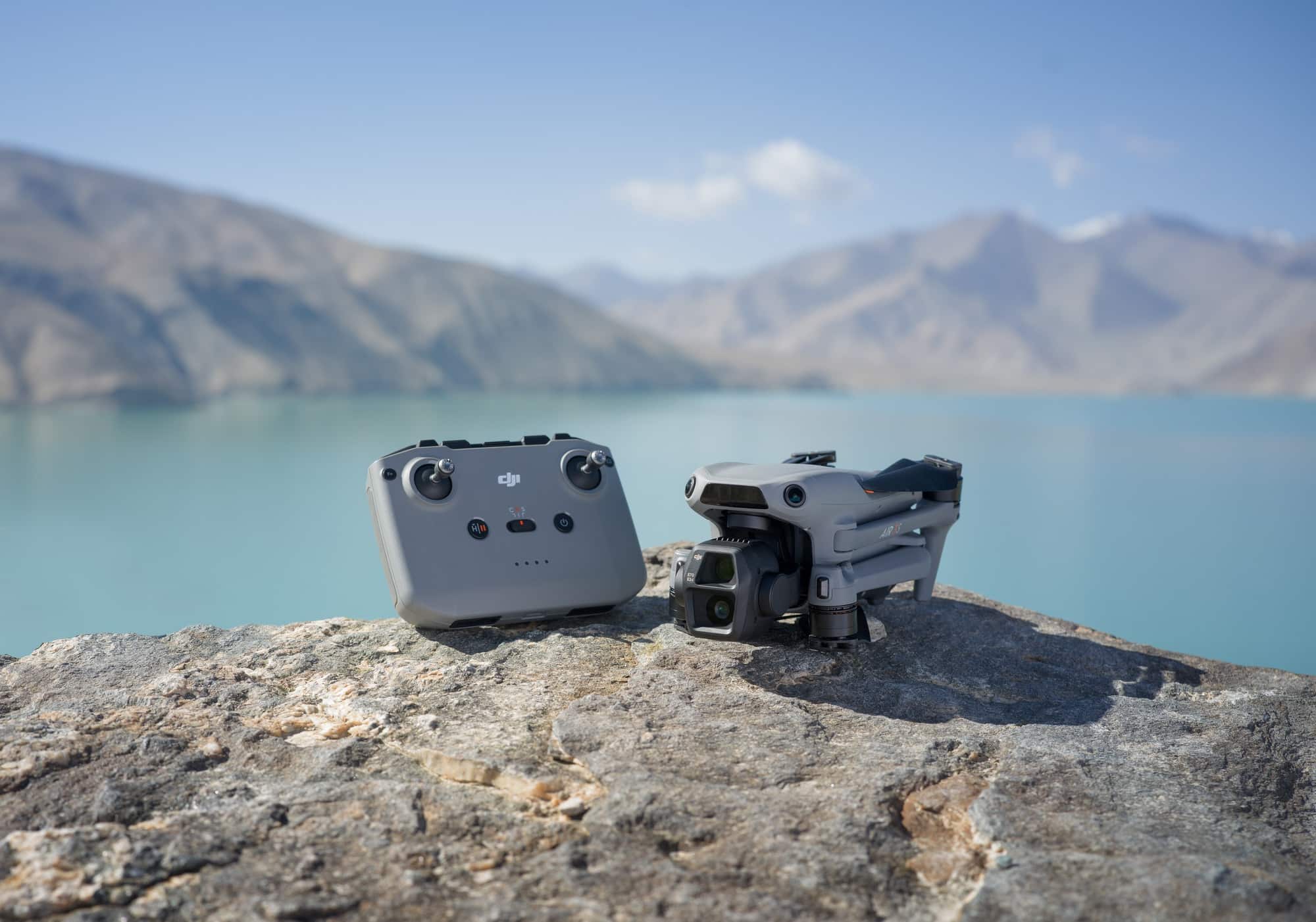 RC-N3 controller and the folded Air 3S on a rock above a turquoise lake.