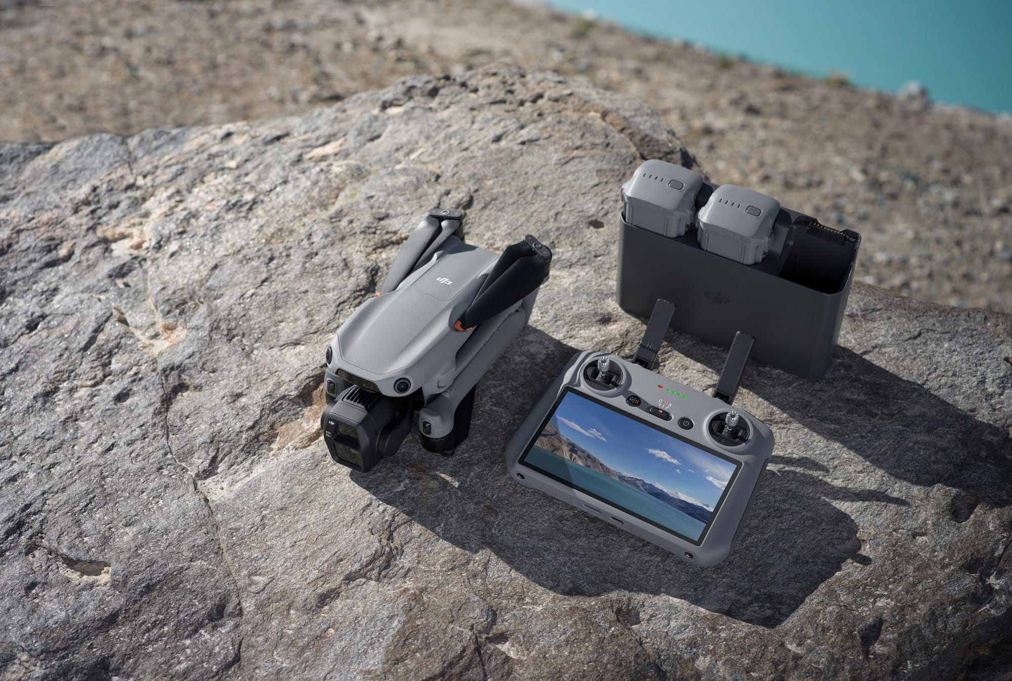 A folded DJI Air 3S on rock beside its controller and two-battery charging hub.