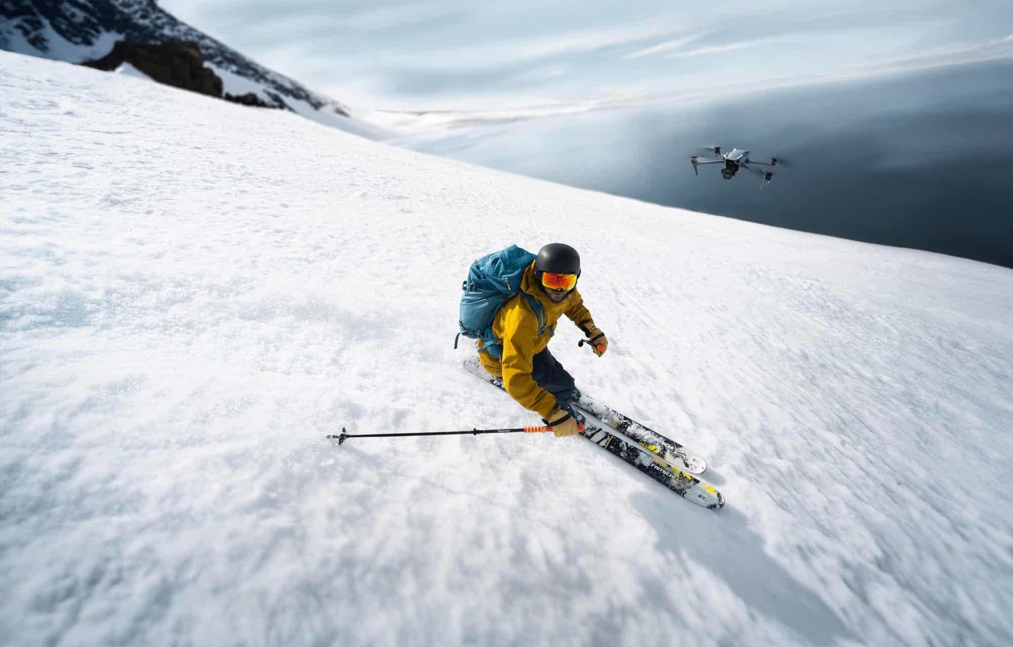 Skier in yellow carves an open snow slope as the drone tracks from behind.