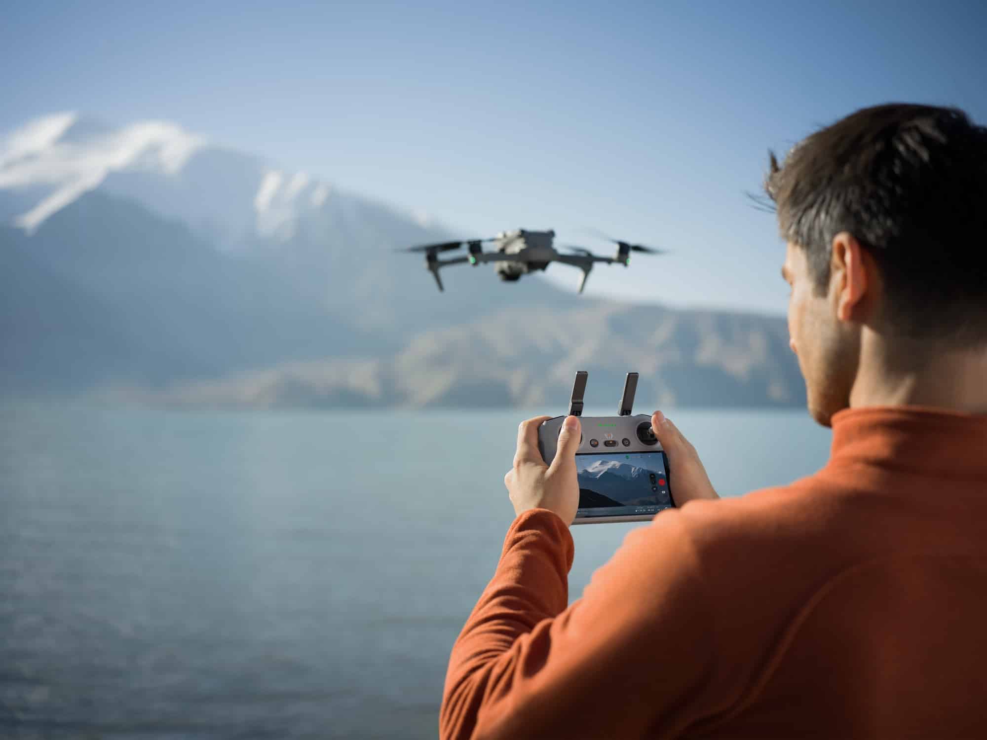 Man in orange holds the RC 2 controller while the drone hovers over a lake.