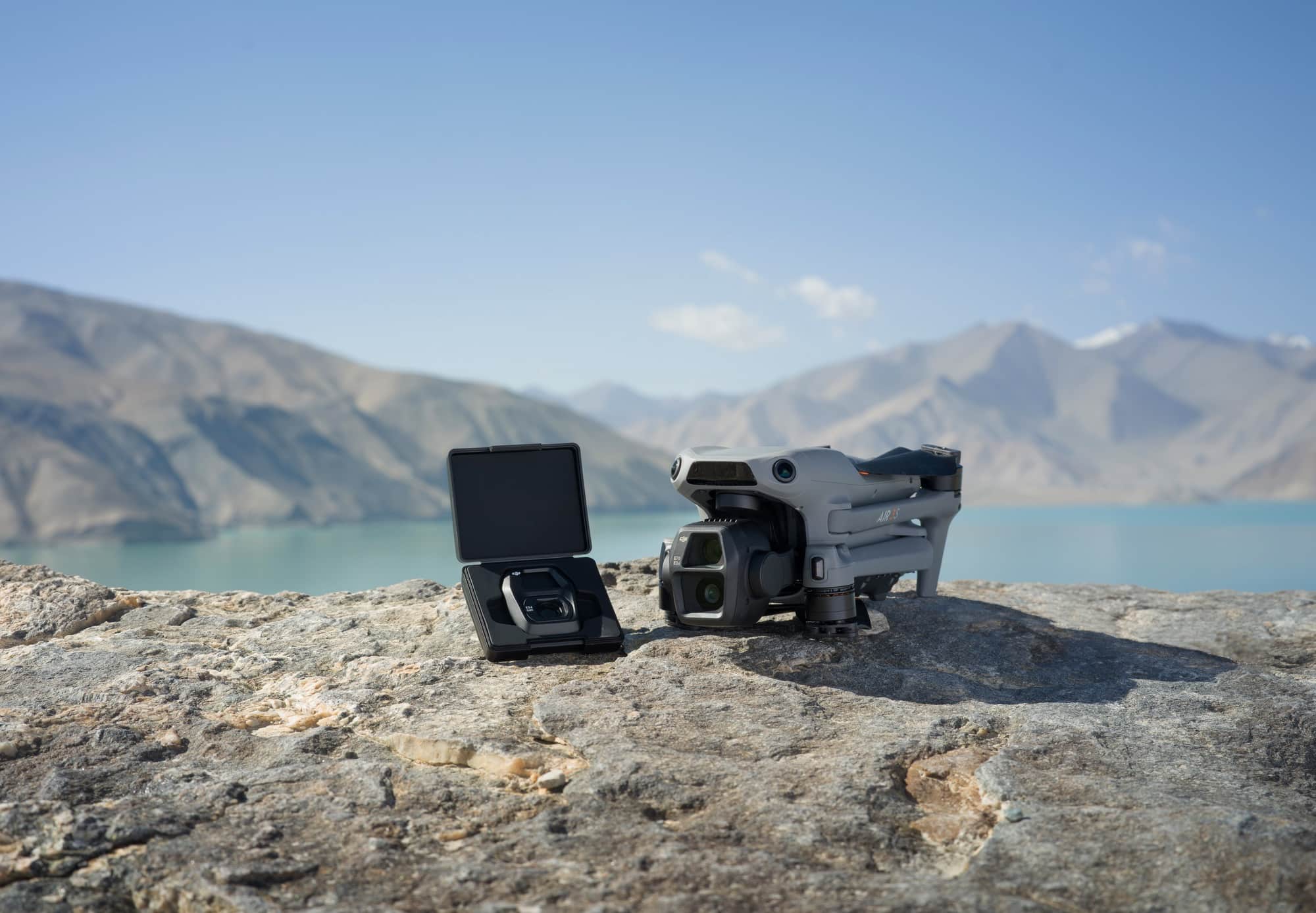 Open accessory case beside the folded Air 3S on a rock above the lake.