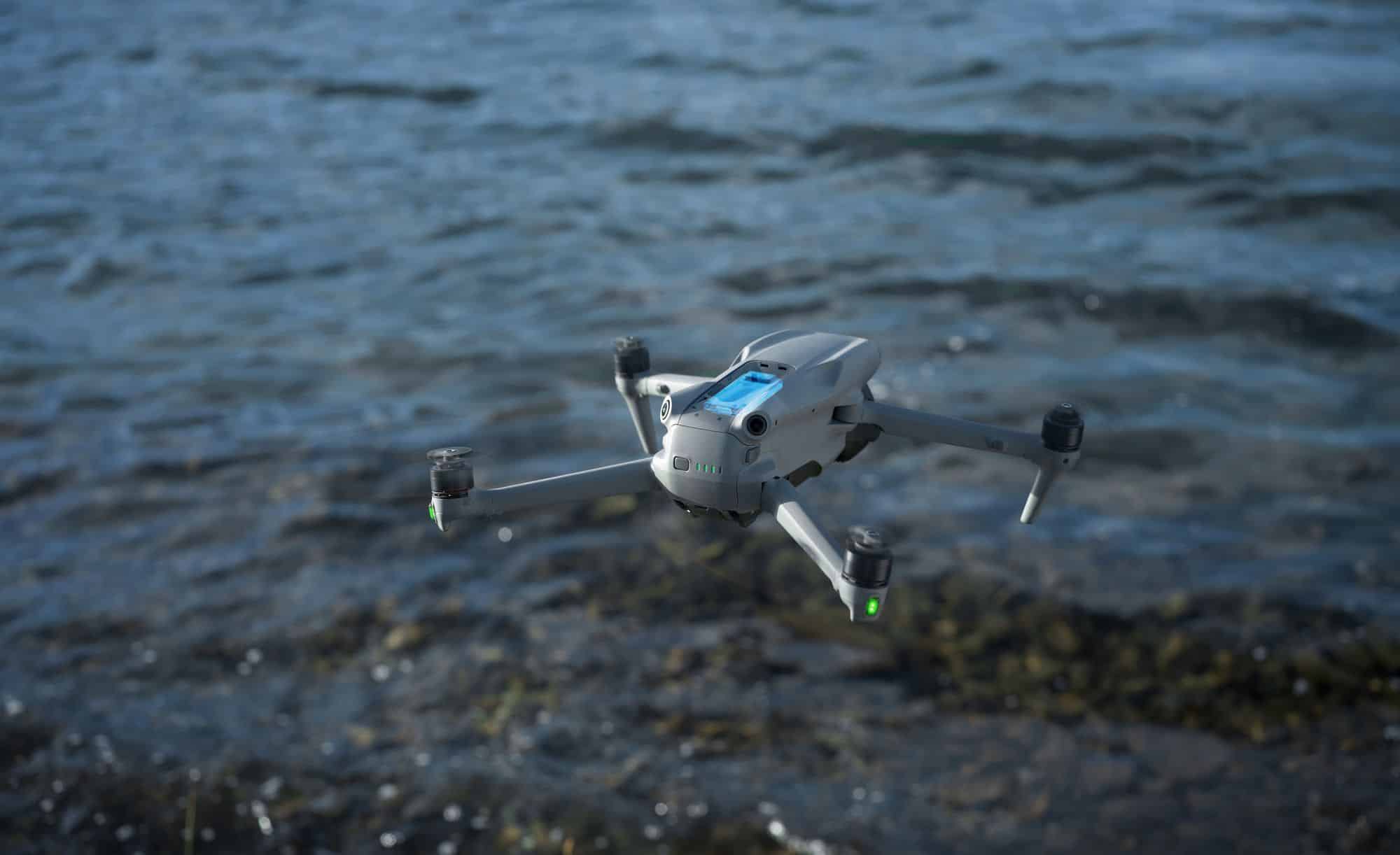 Air 3S skims low over dark rippling water beside a rocky shoreline.