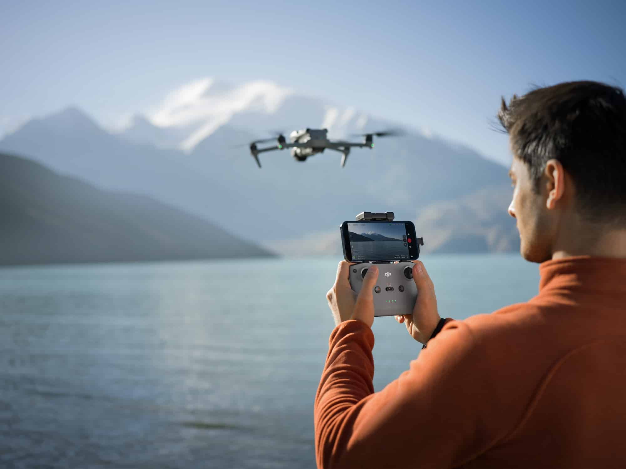Man in orange holds an RC-N3 with phone attached as the drone hovers ahead.