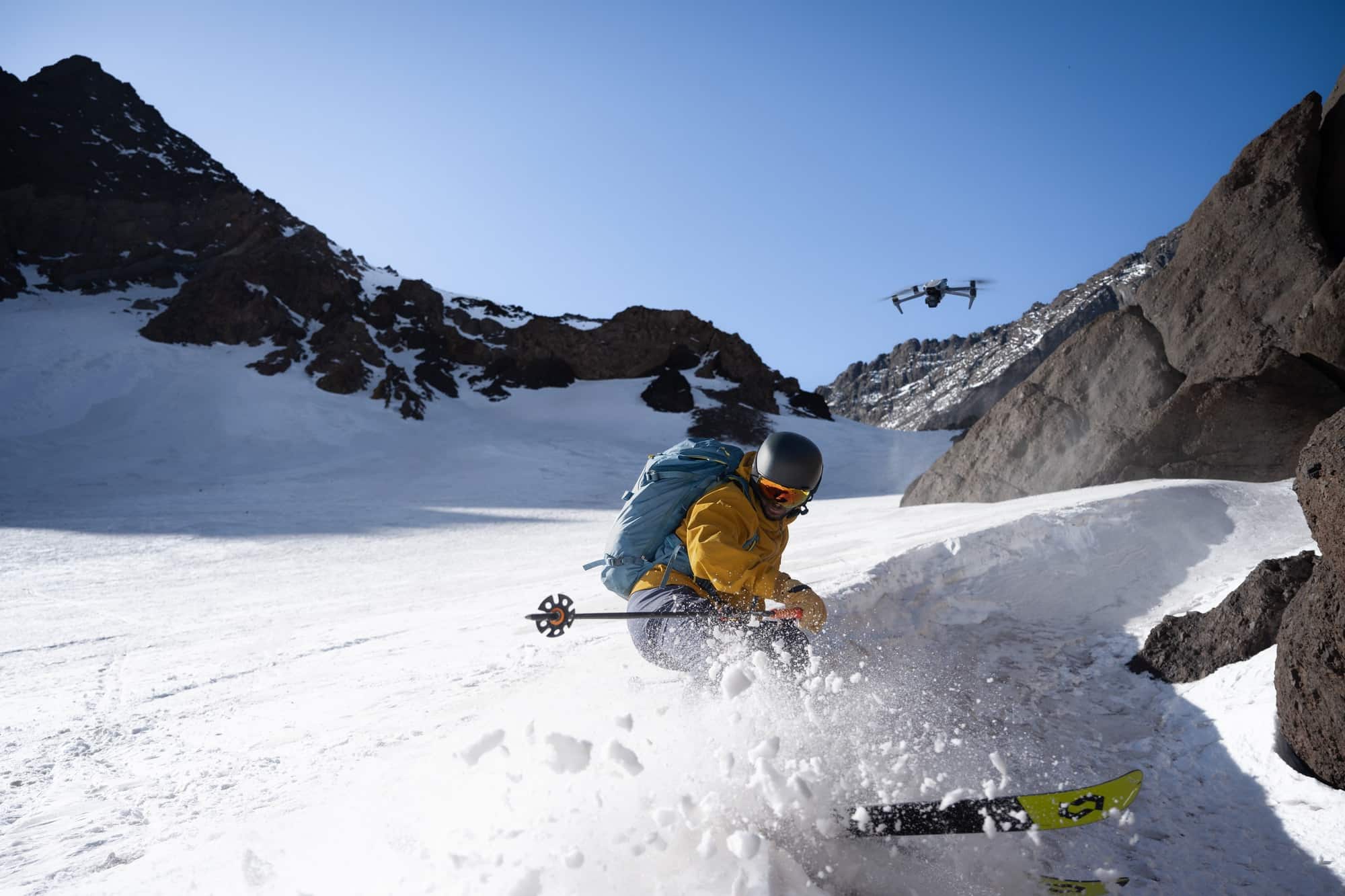 Skier carves through fresh snow as the Air 3S tracks overhead between rock walls.