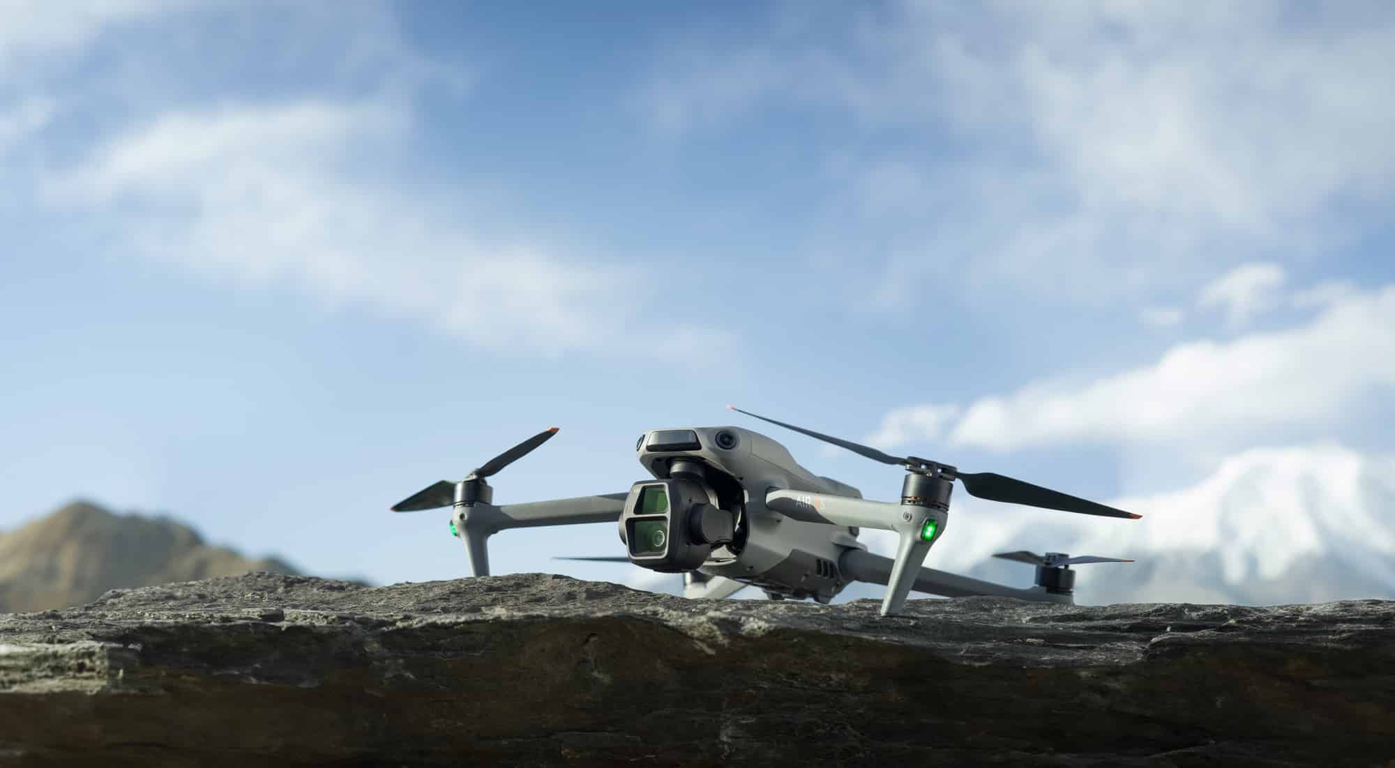 A DJI Air 3S perched on a mossy rock before a snowy peak.