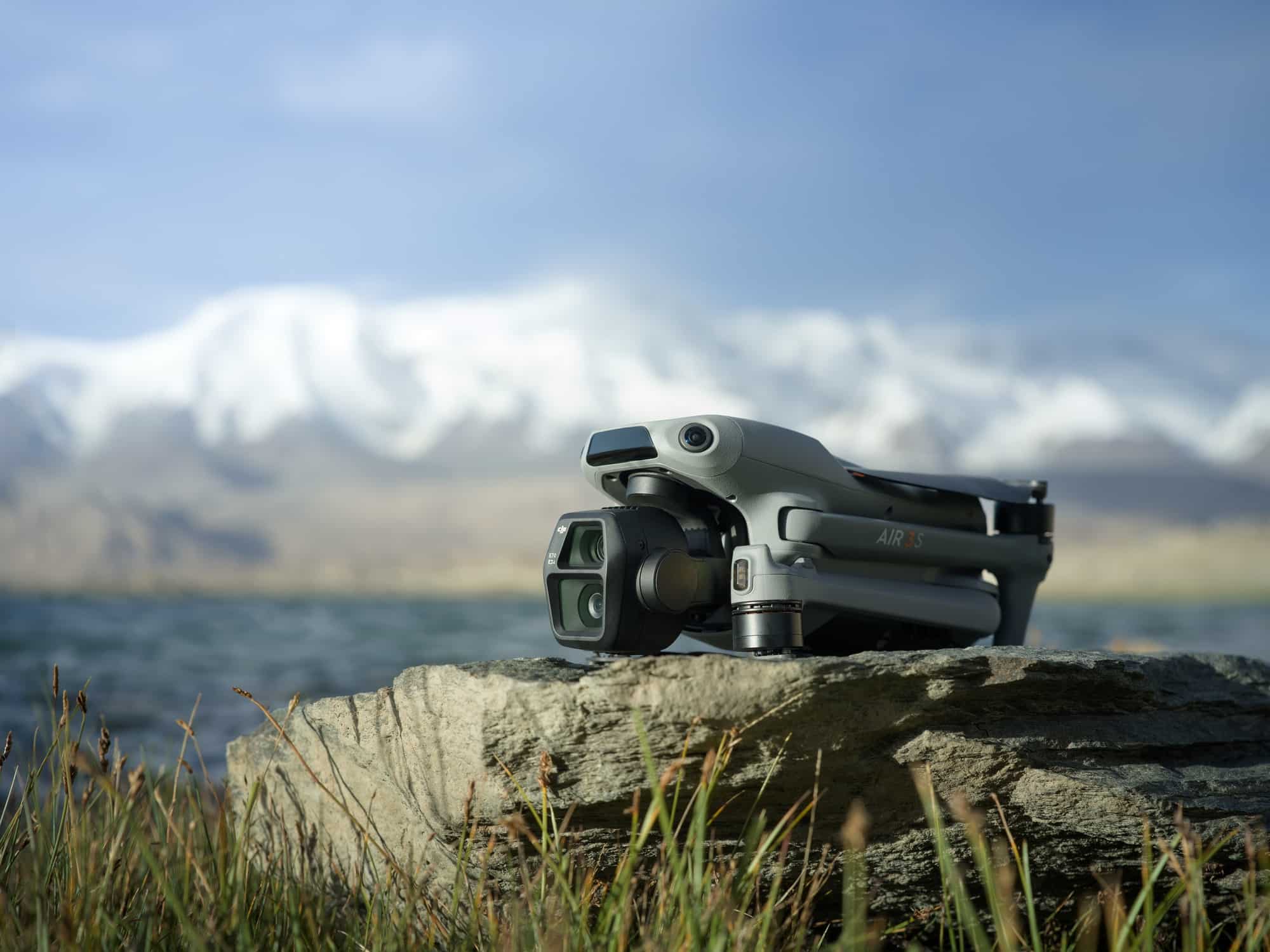 Air 3S standing on a grassy rock ledge with a snow-capped peak behind.