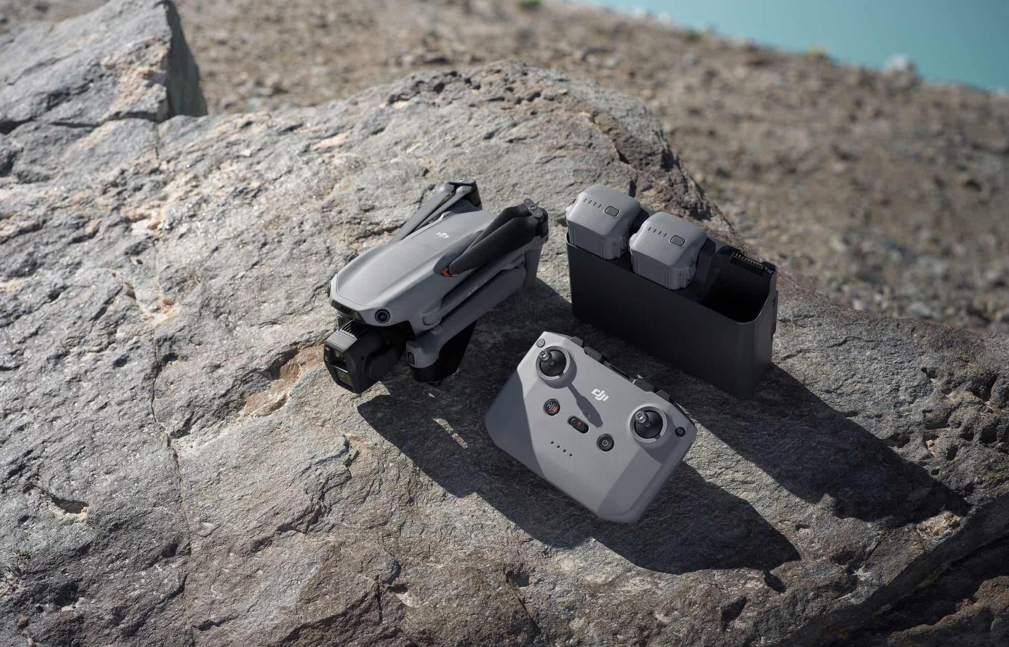 Folded drone, RC 2 controller and battery hub laid out on a sunlit rock.