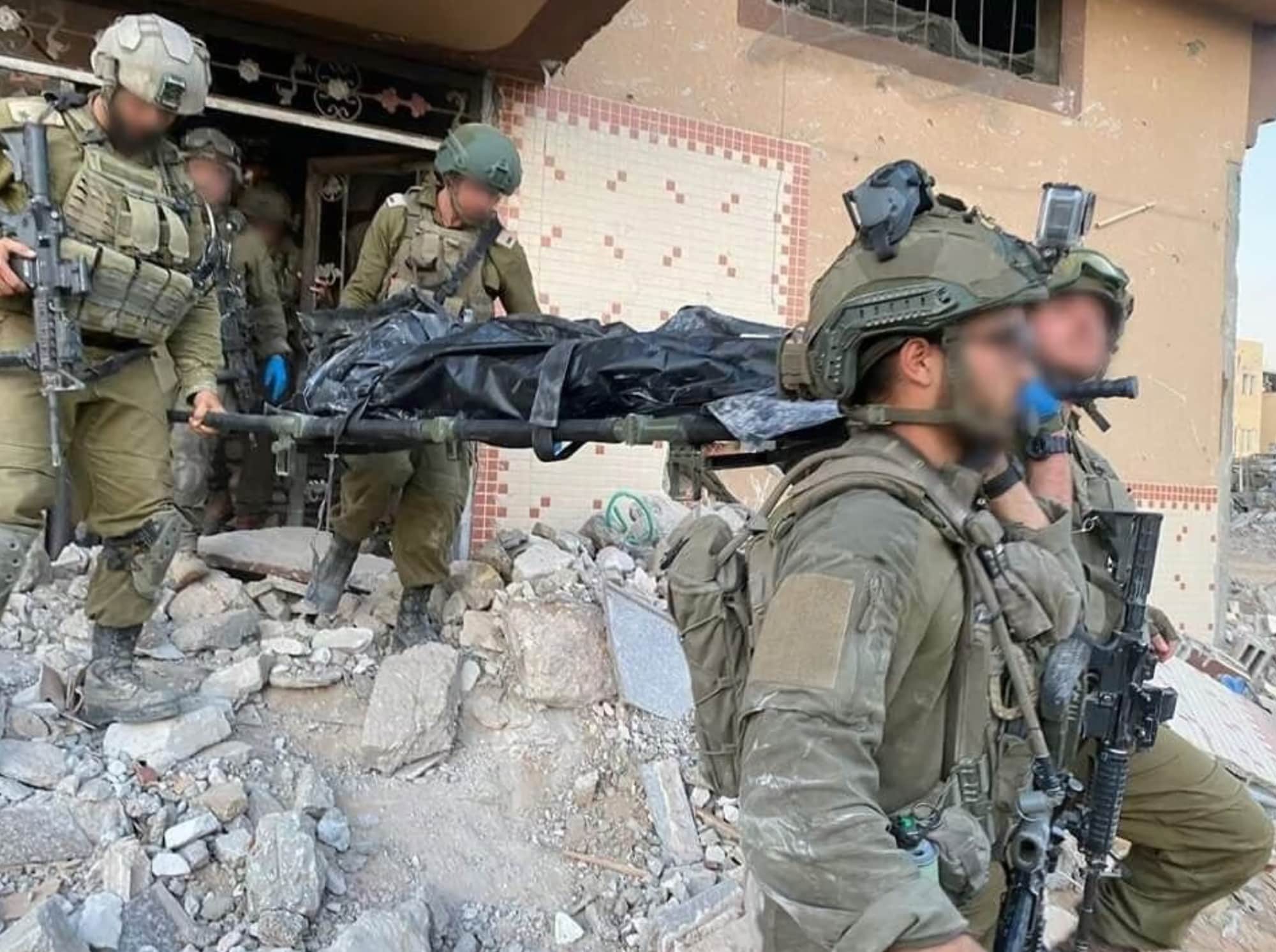 Soldiers carry a covered body on a stretcher across rubble.