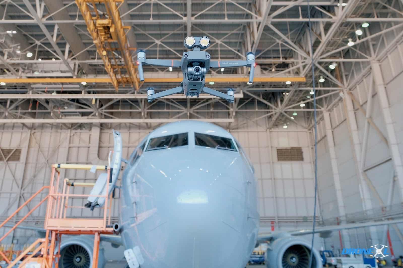 Inspection drone hovering in front of an airliner nose inside a maintenance hangar.