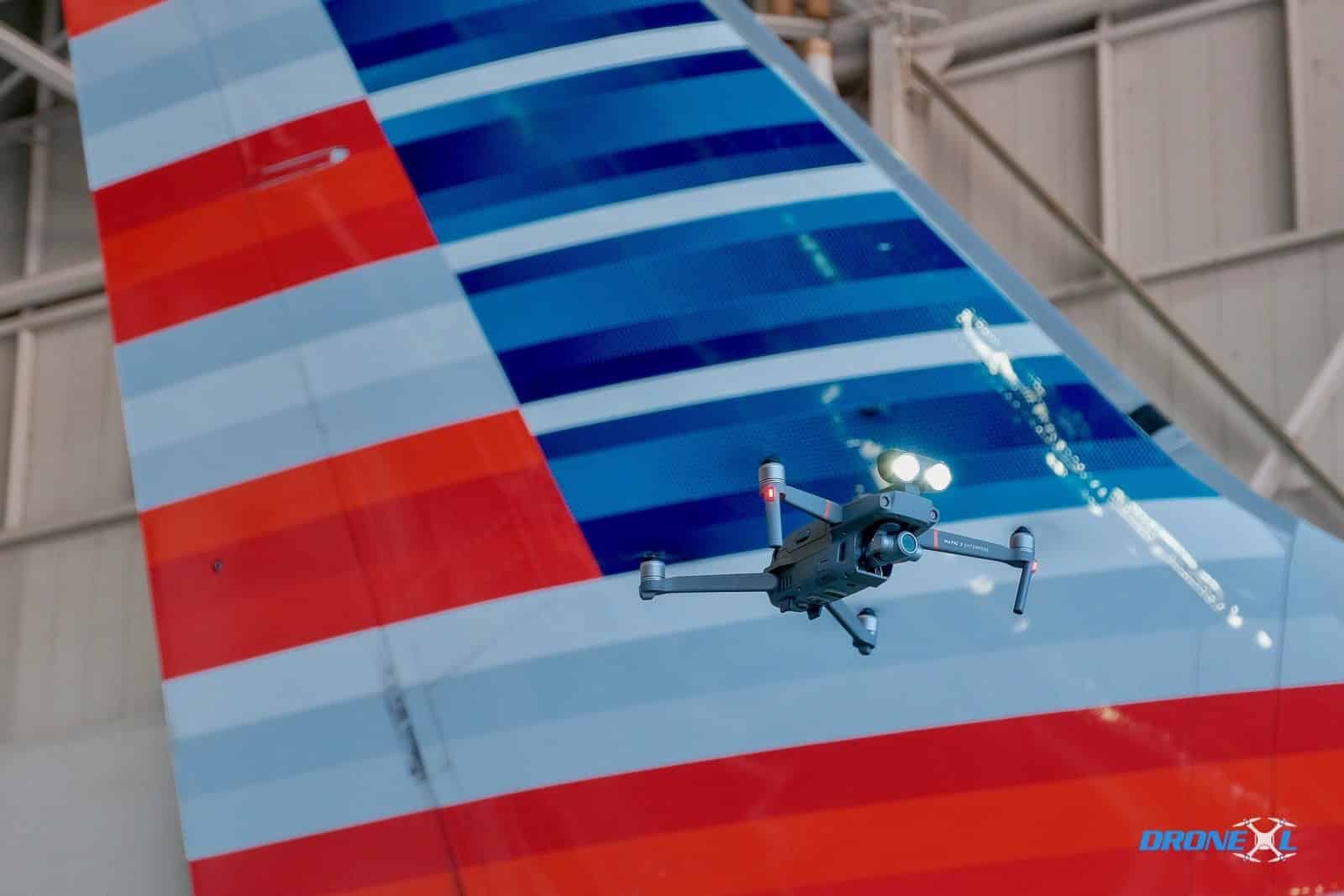 Inspection drone hovering beside the striped tail of an American Airlines jet.