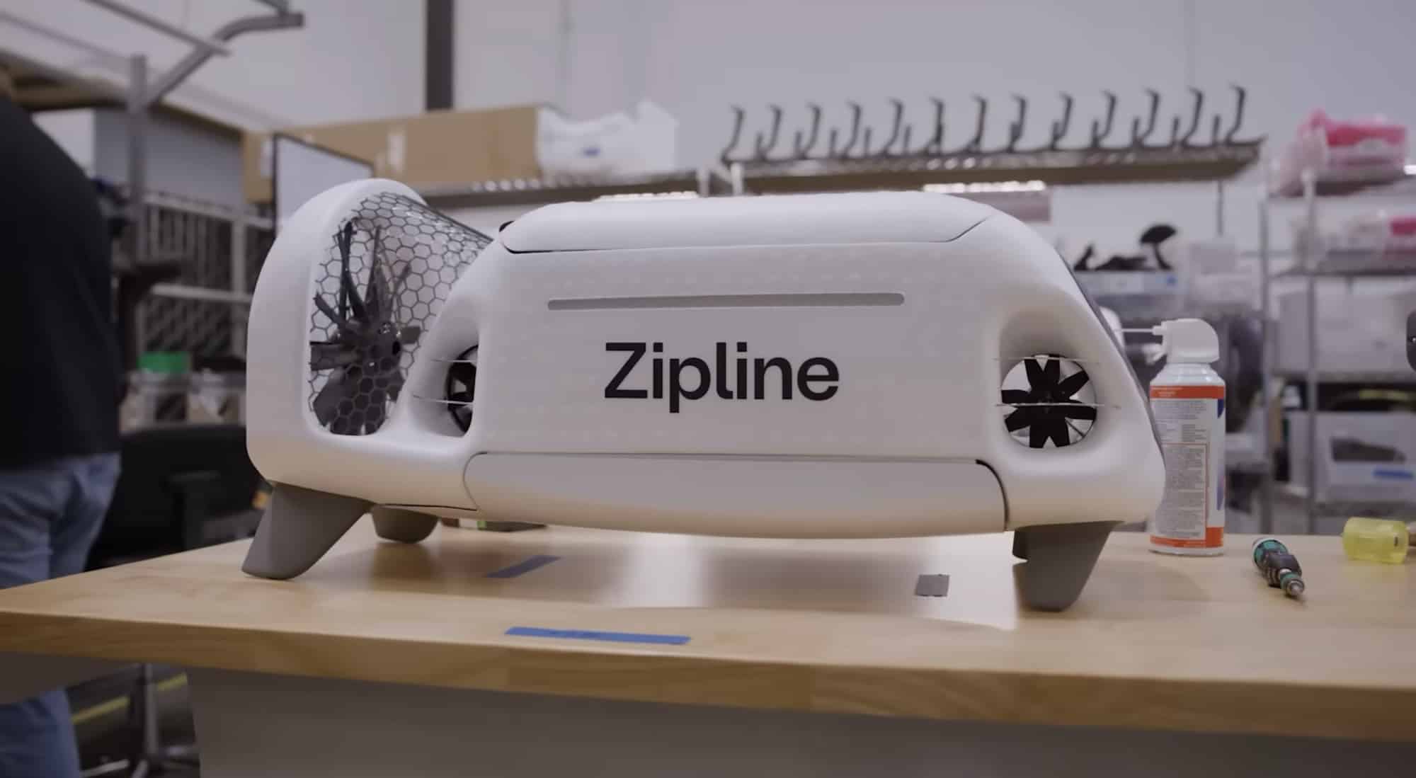 Zipline aircraft resting on a workbench in a workshop with parts shelving behind it.