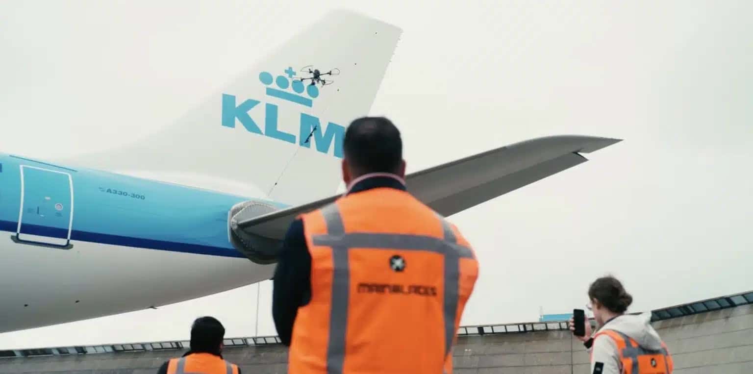 Ground crew in orange vests watching a drone inspect a KLM aircraft tail.