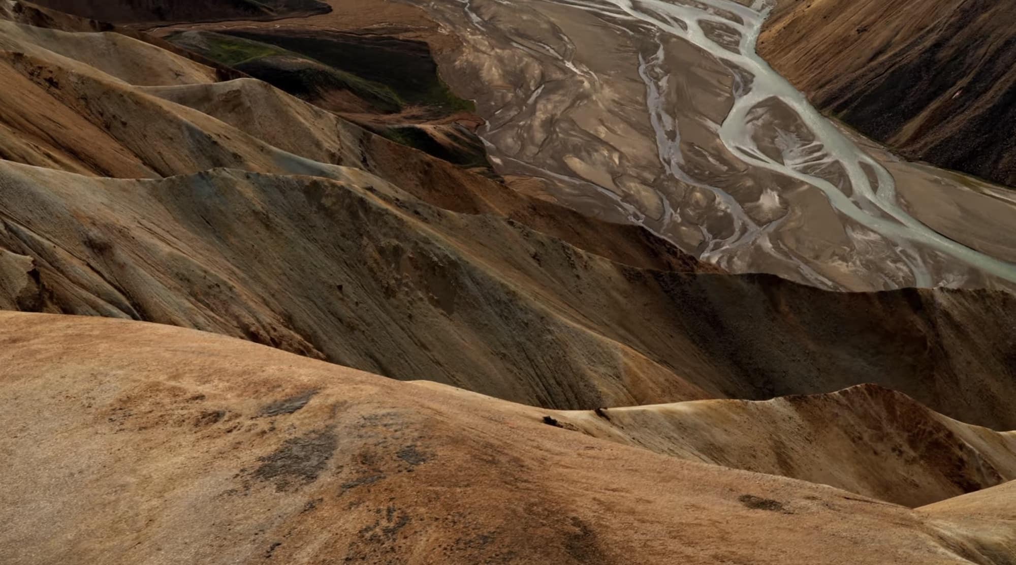 Braided glacial river winding through rust-colored Icelandic highlands from above.