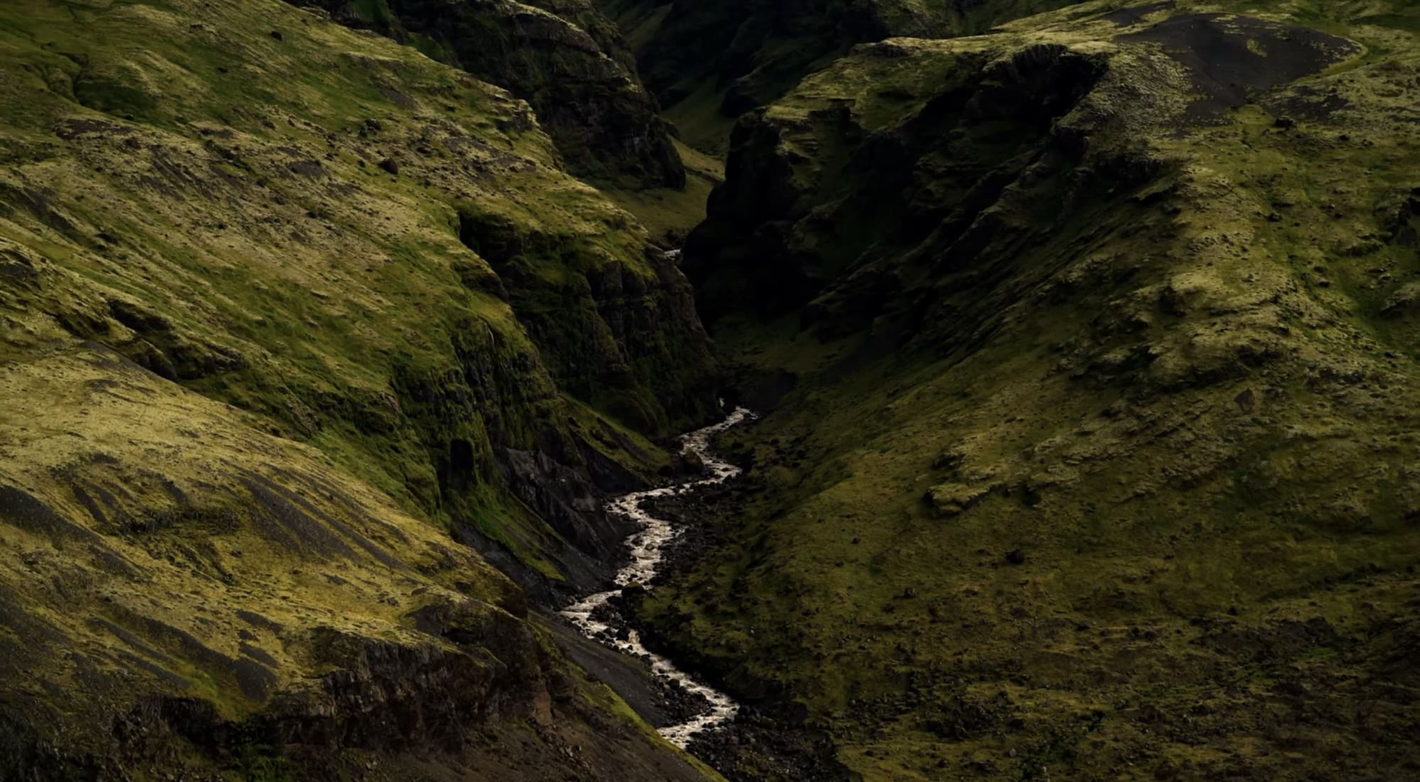 Aerial view of a narrow river cutting through steep moss-covered Arctic slopes.