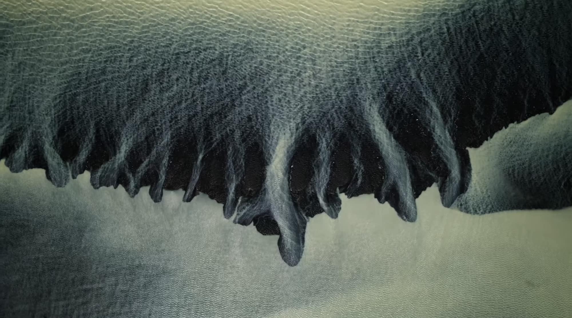 Dark sediment fanning out into a pale glacial lagoon seen from above.