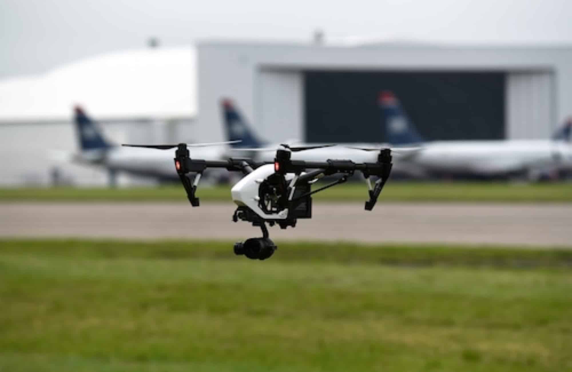 DJI Inspire hovering over grass with airliners parked outside a hangar.