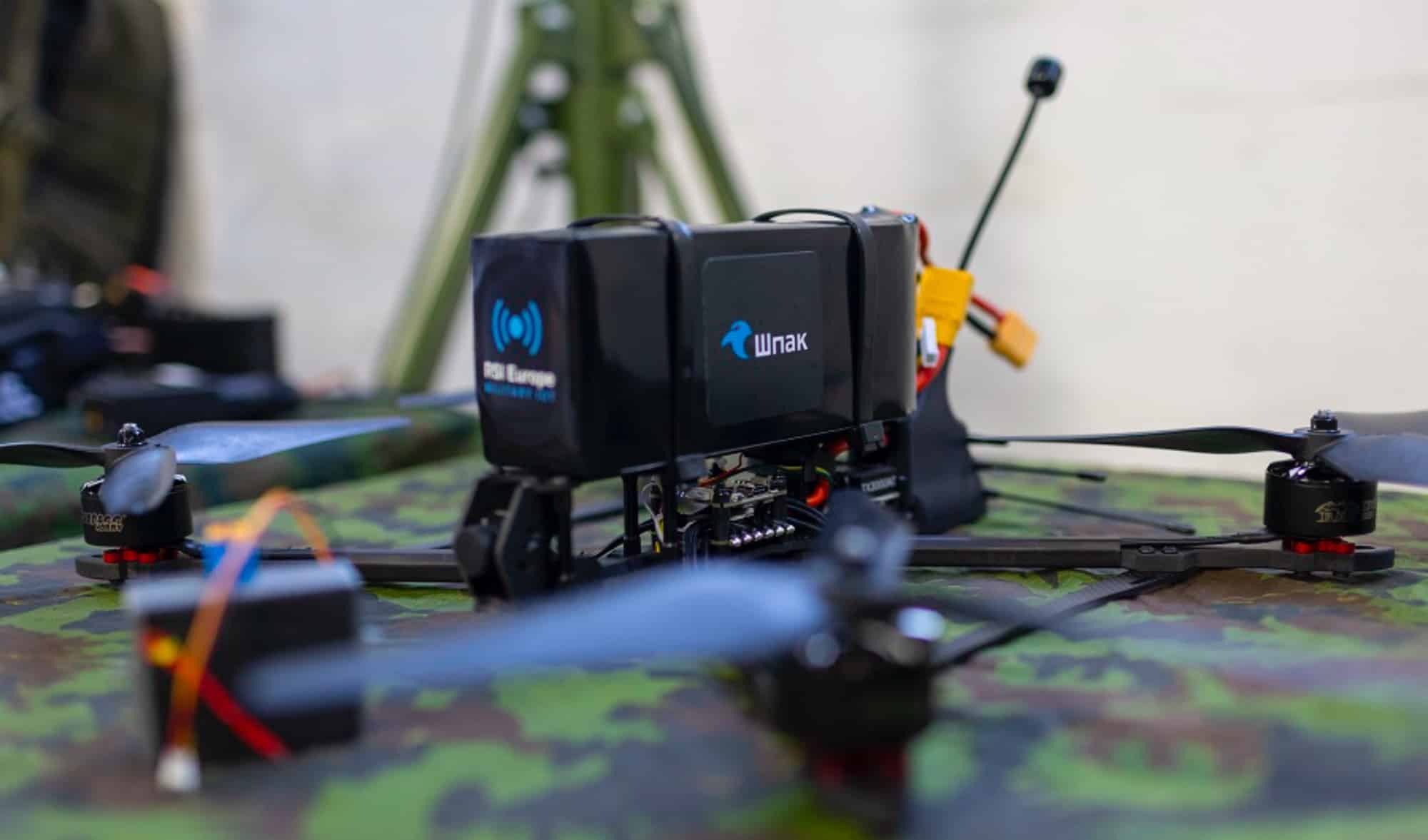 Shpak FPV quadcopter fitted with an RSI Europe module on camouflage netting.