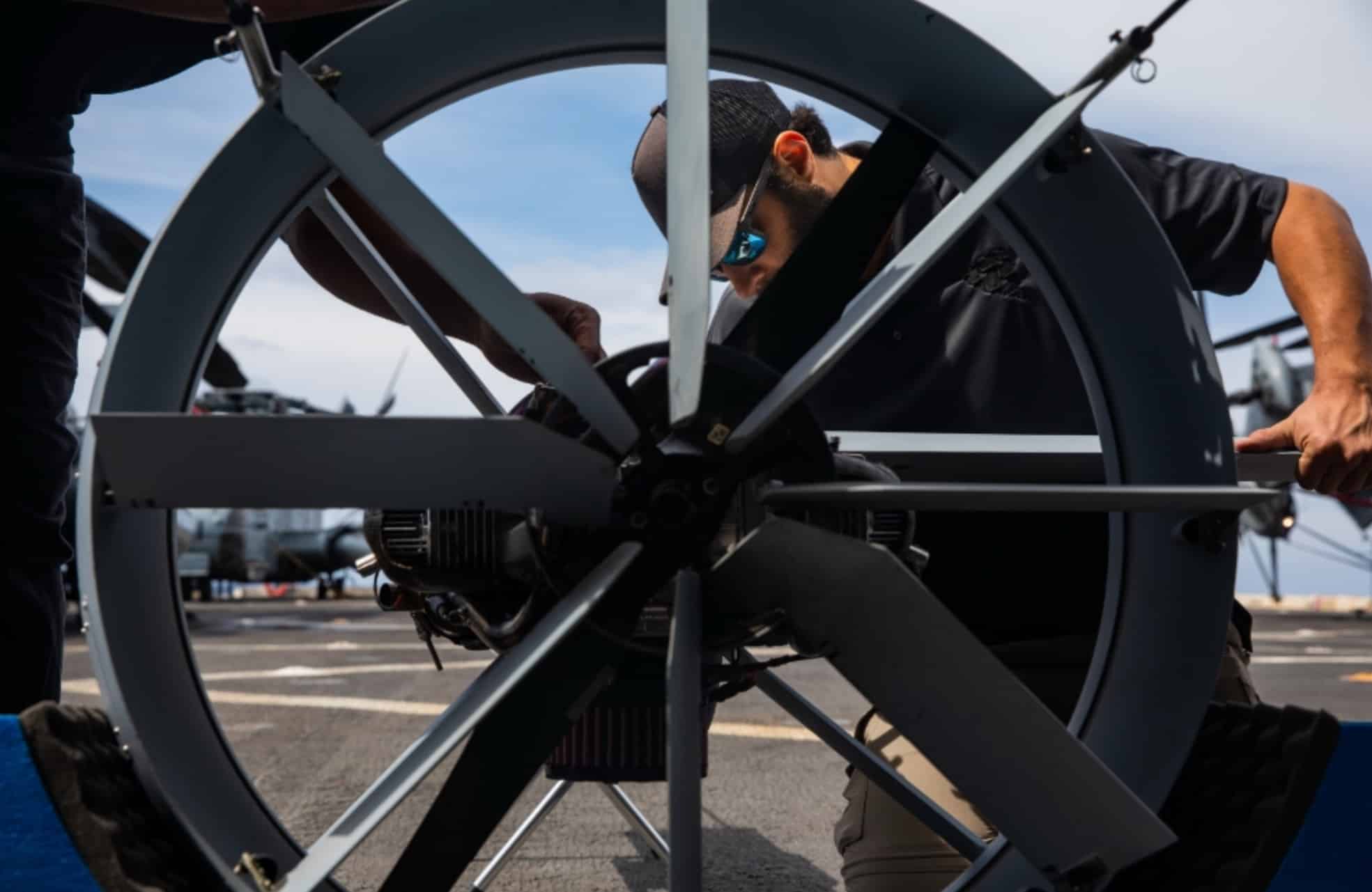 A technician in sunglasses adjusting a large ducted propeller assembly outdoors.