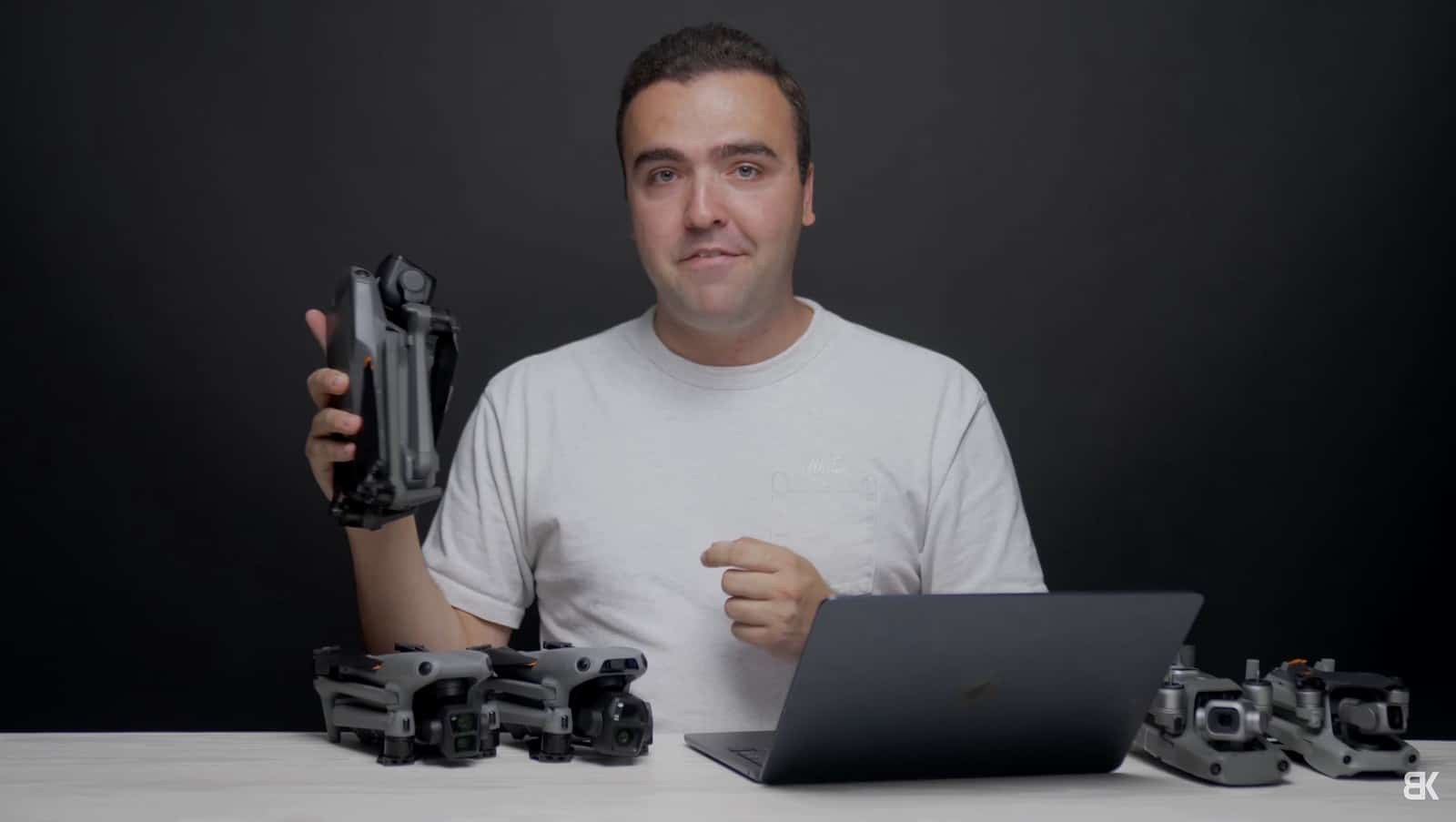 Reviewer Billy holding a folded drone at a desk lined with other DJI models.