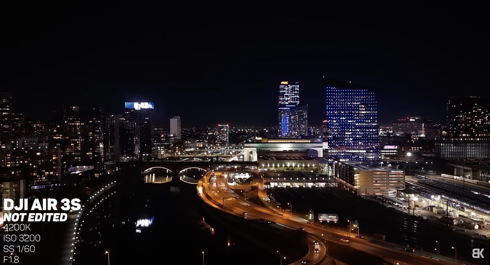 Night aerial over a lit riverfront and rail yard shot at ISO 3200.