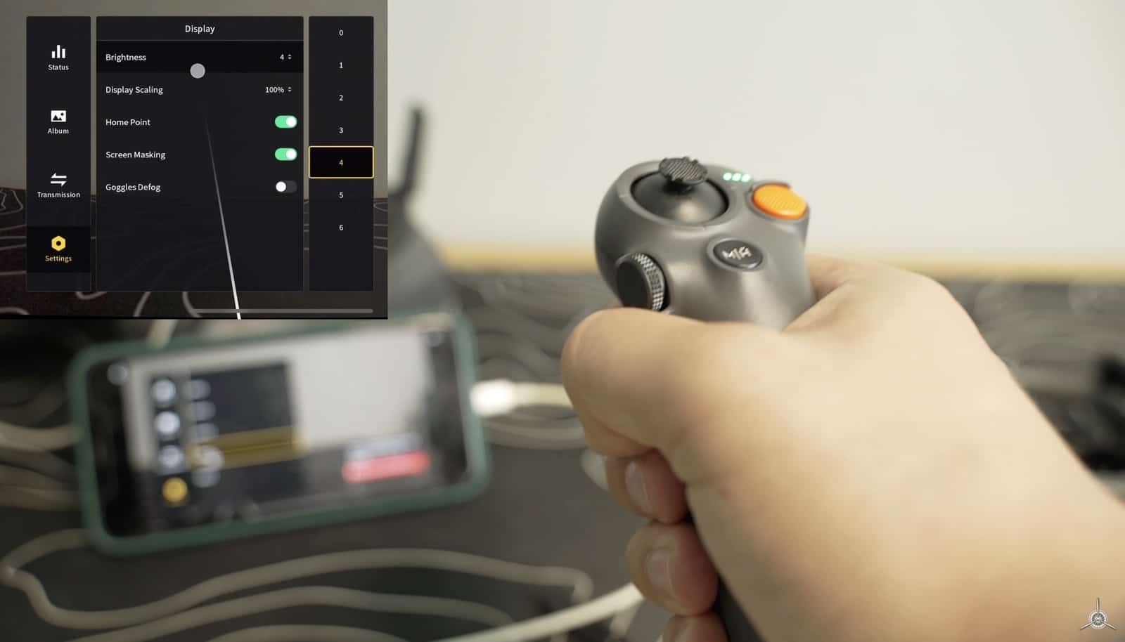 Hand on a DJI motion controller with the goggles display settings menu shown behind.