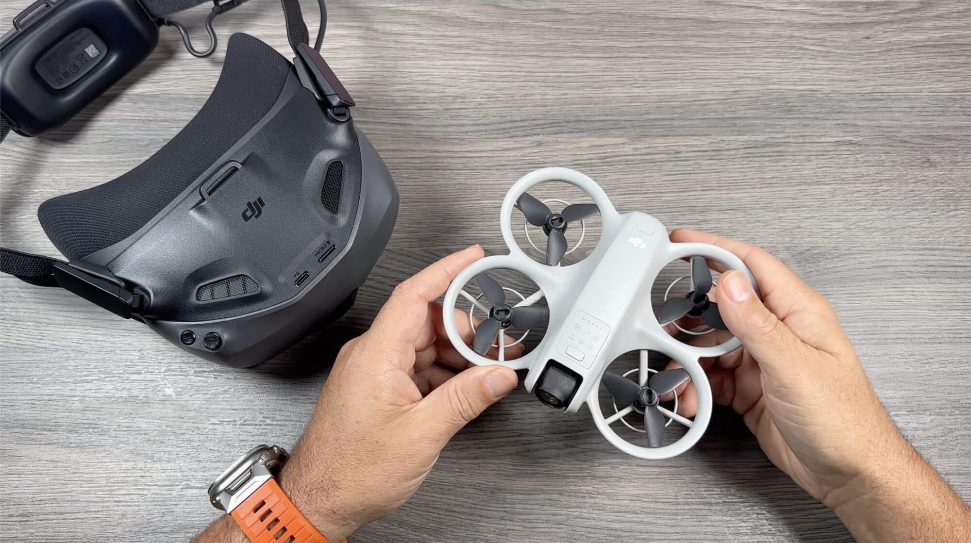Hands holding a white DJI Neo next to DJI goggles on a table.
