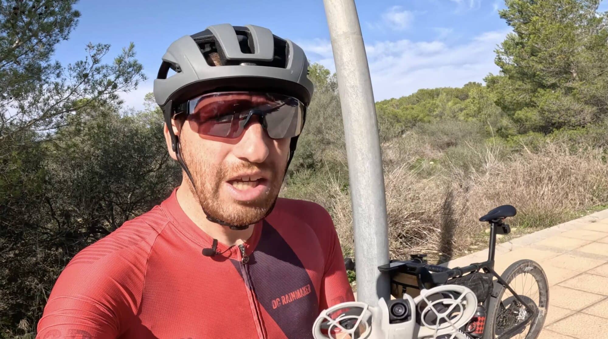 Cyclist in helmet and sunglasses beside a bicycle and small tracking drone.