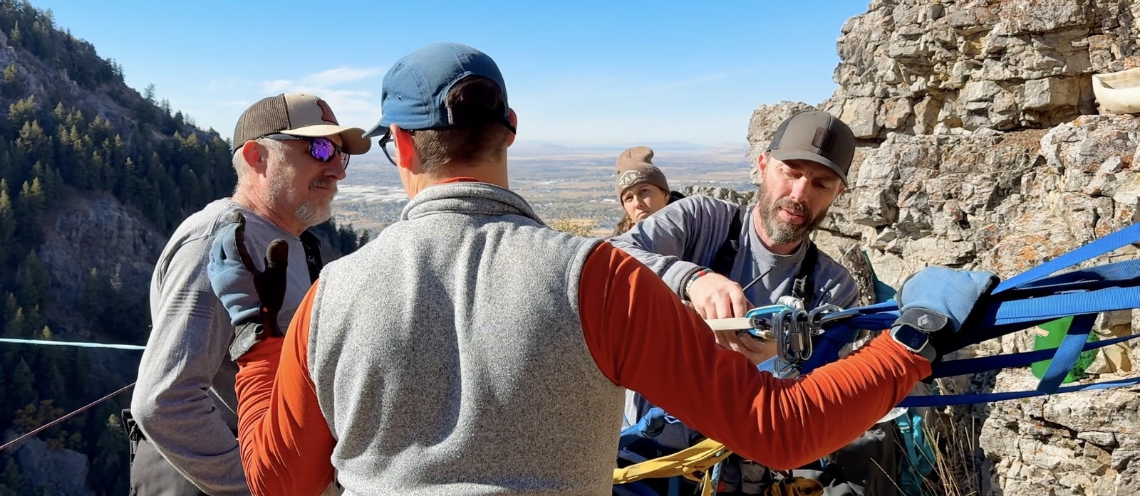 Volunteers in caps rigging rope hardware and pulleys on a rocky ledge.