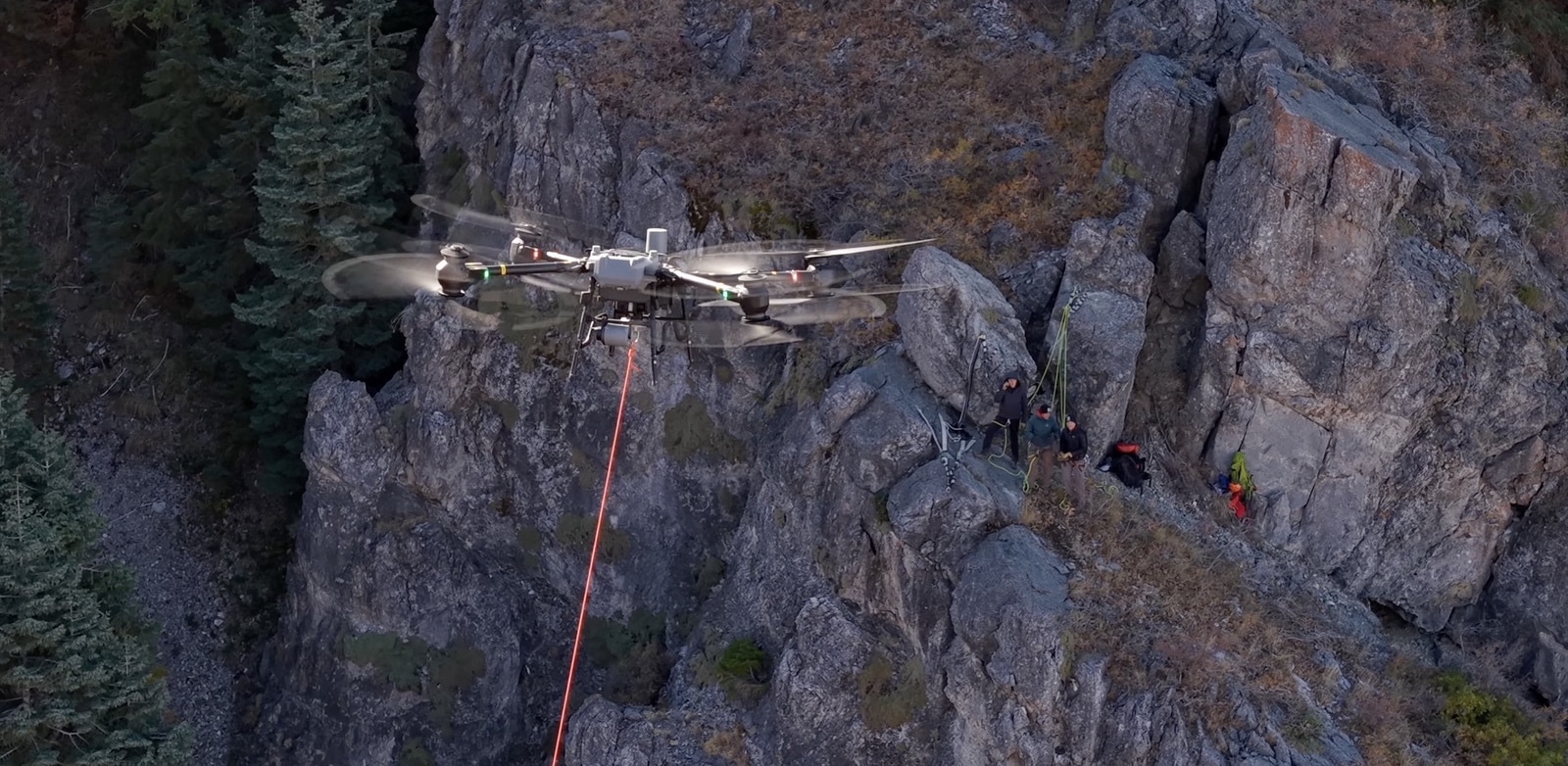 FlyCart 30 hovering beside a rock face with a red rope and crew below.