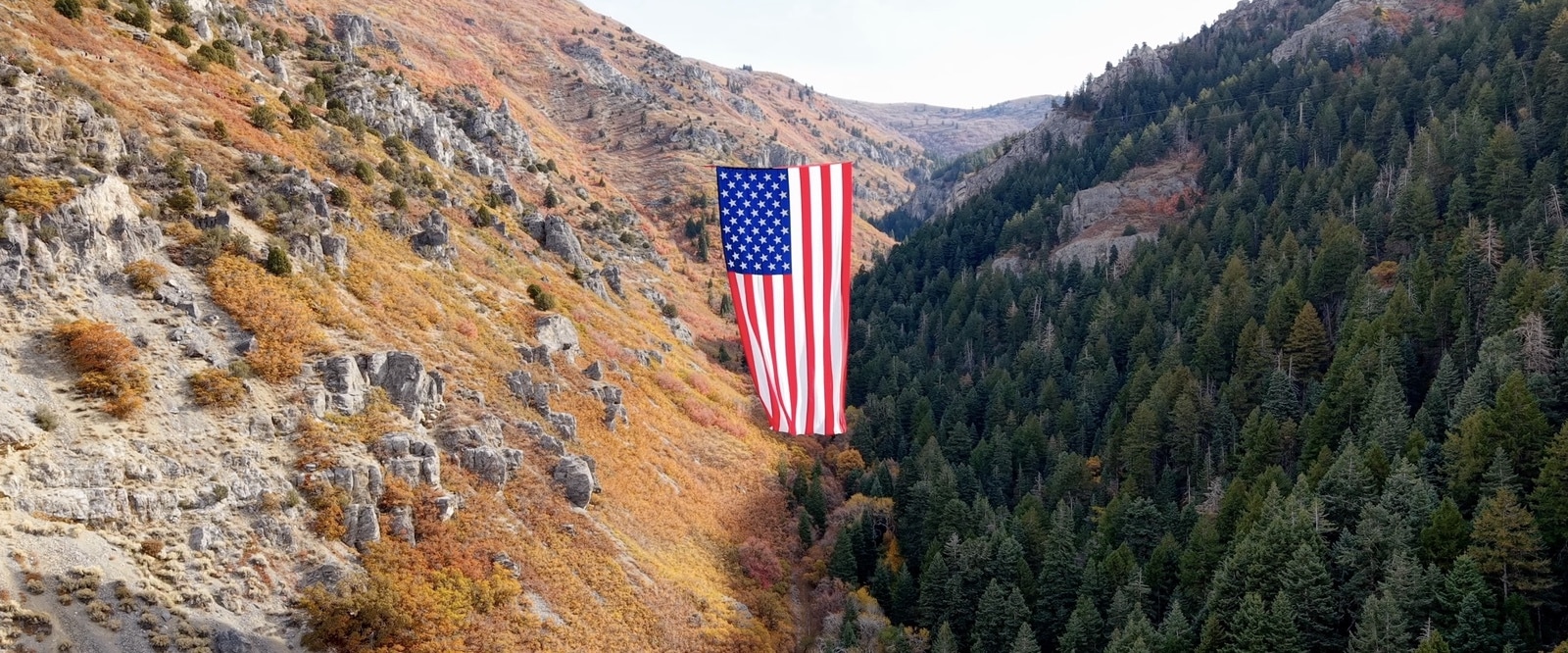 The unfurled flag hanging between forested canyon walls after the Veterans Day release.